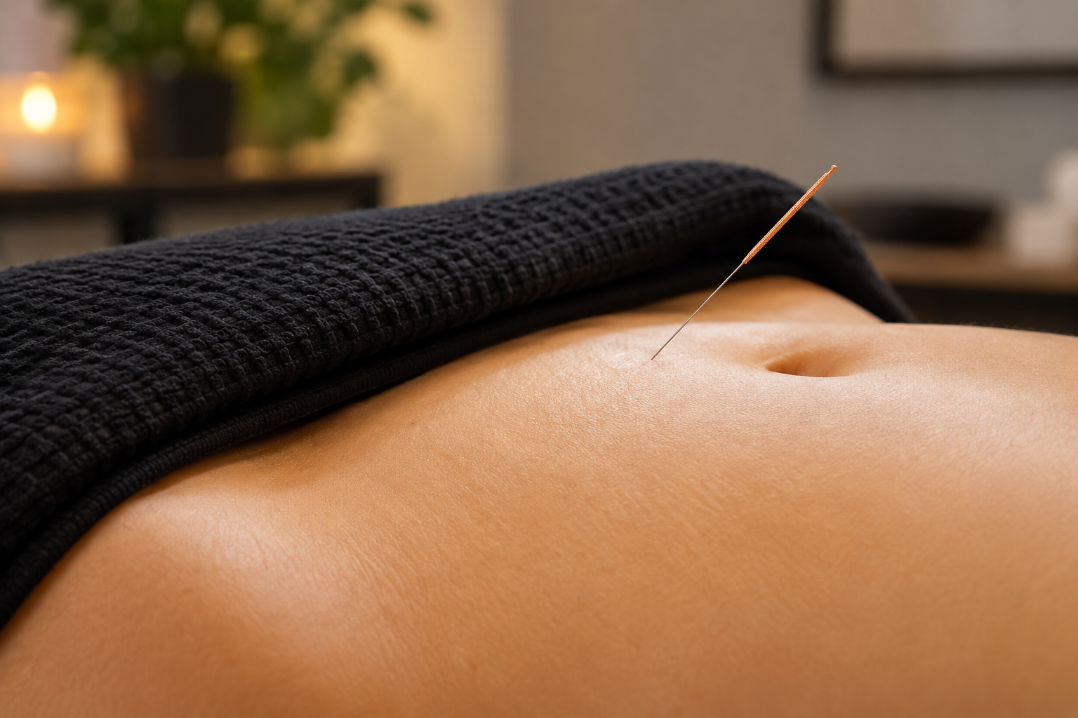 Close-up of a person's abdomen with an acupuncture needle inserted into the skin during a therapy session.