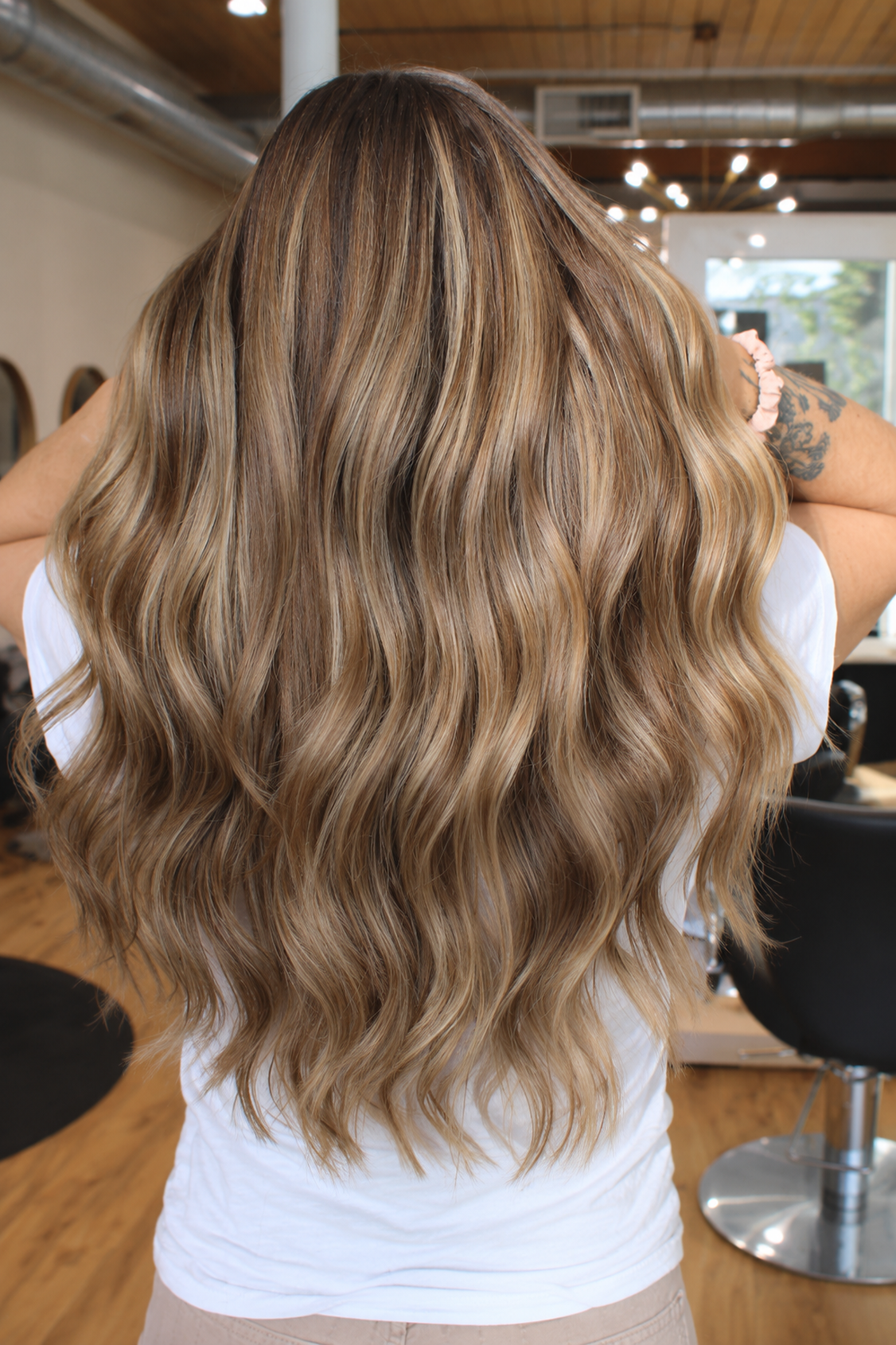 Soft blonde balayage and highlights on long wavy hair at Raven Hair Studio in Palmer, AK