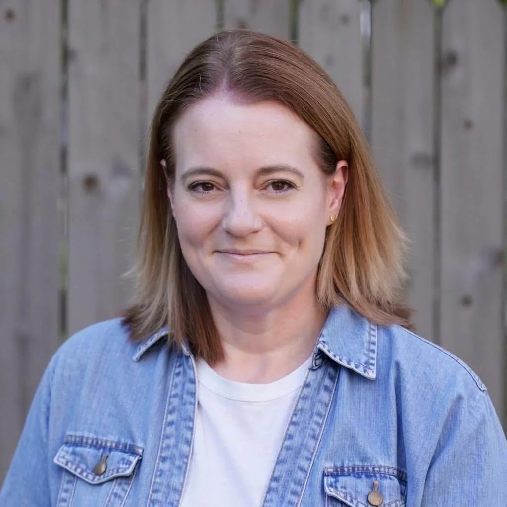 Jennifer Campbell standing against a fence dressed in a blue shirt and white T-shirt