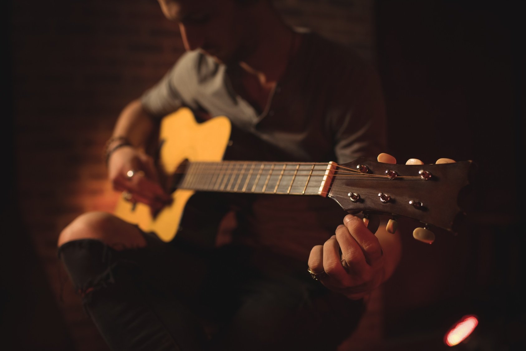 A person playing an acoustic guitar in a dimly lit room.