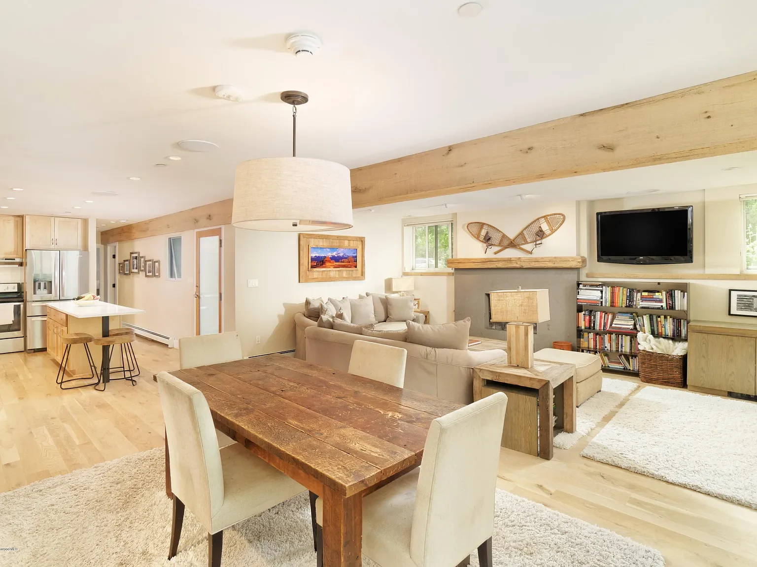 Spacious open-concept living and dining area featuring exposed wood beams, stone fireplace, and built-in library shelves in Aspen, Colorado.