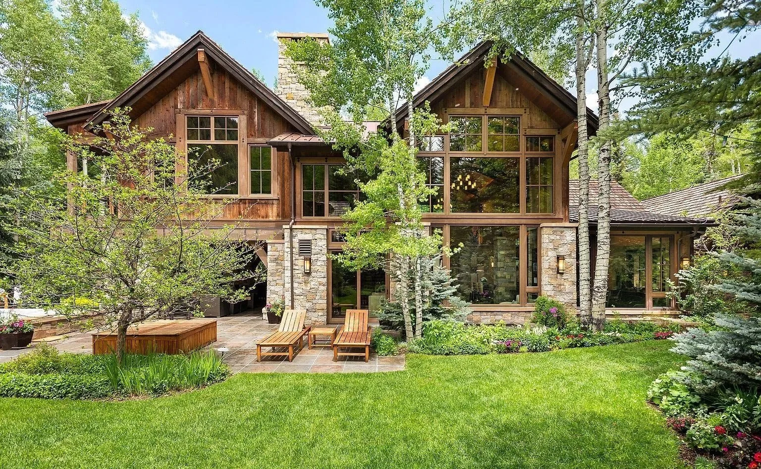 A spacious and elegant two-story stone and wood home with large windows surrounded by trees and wildflowers built by John Olson, owner of Form 44 Construction, on Crystal Lake Road in Aspen, Colorado.