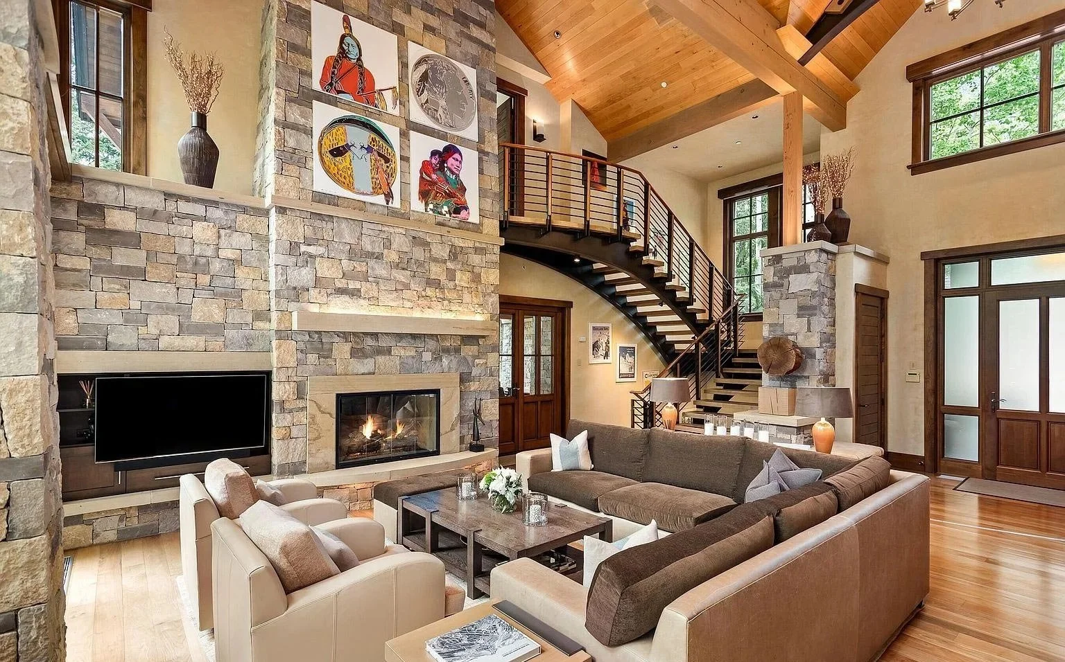 A cozy, luxurious living room with a stone fireplace, vaulted ceilings, and an open staircase built by John Olson, owner of Form 44 Construction, on Crystal Lake Road in Aspen, Colorado.