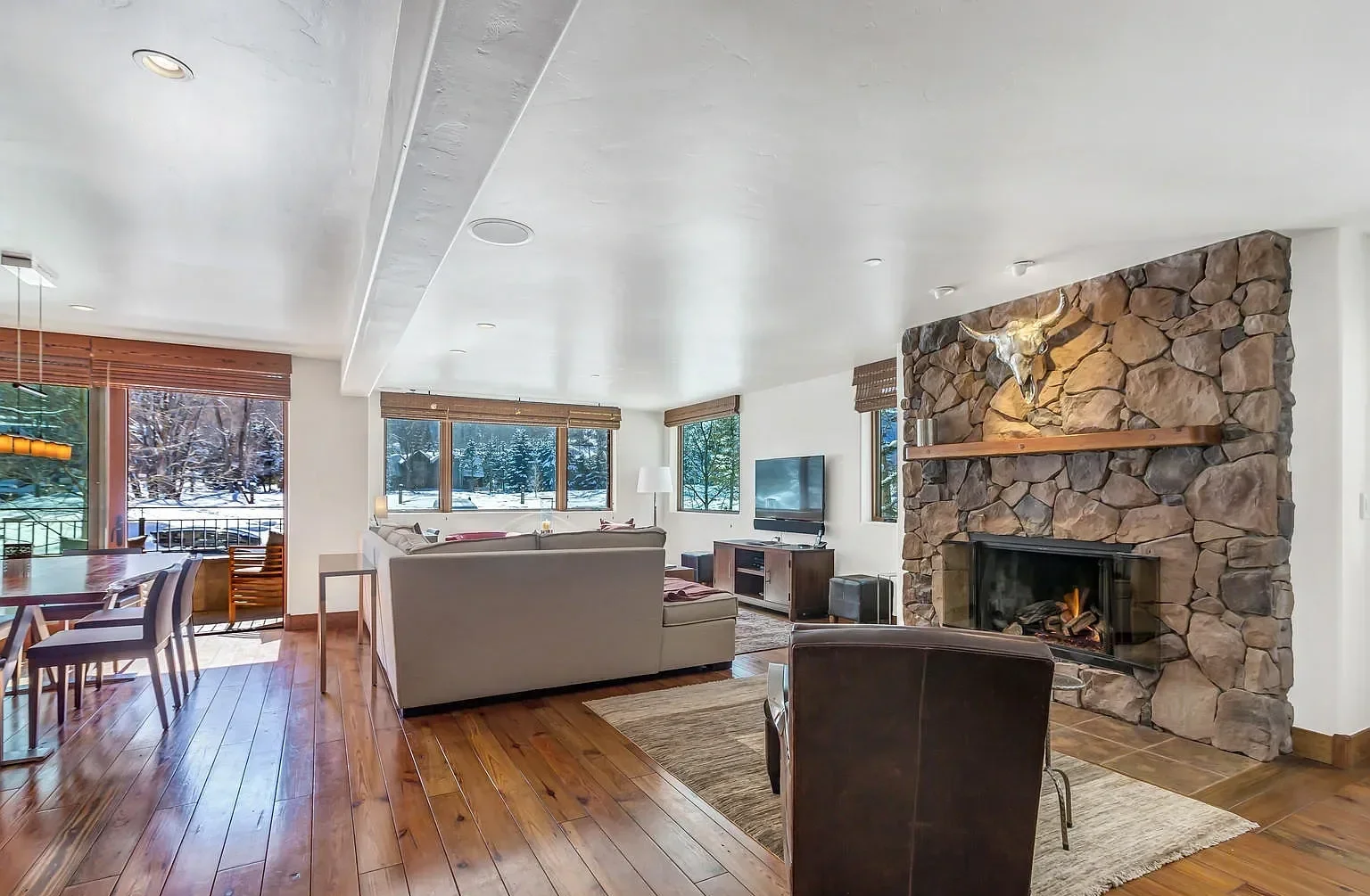 Expansive mountain living room featuring a floor-to-ceiling fieldstone fireplace, hardwood floors, and scenic snow views in Aspen, Colorado.