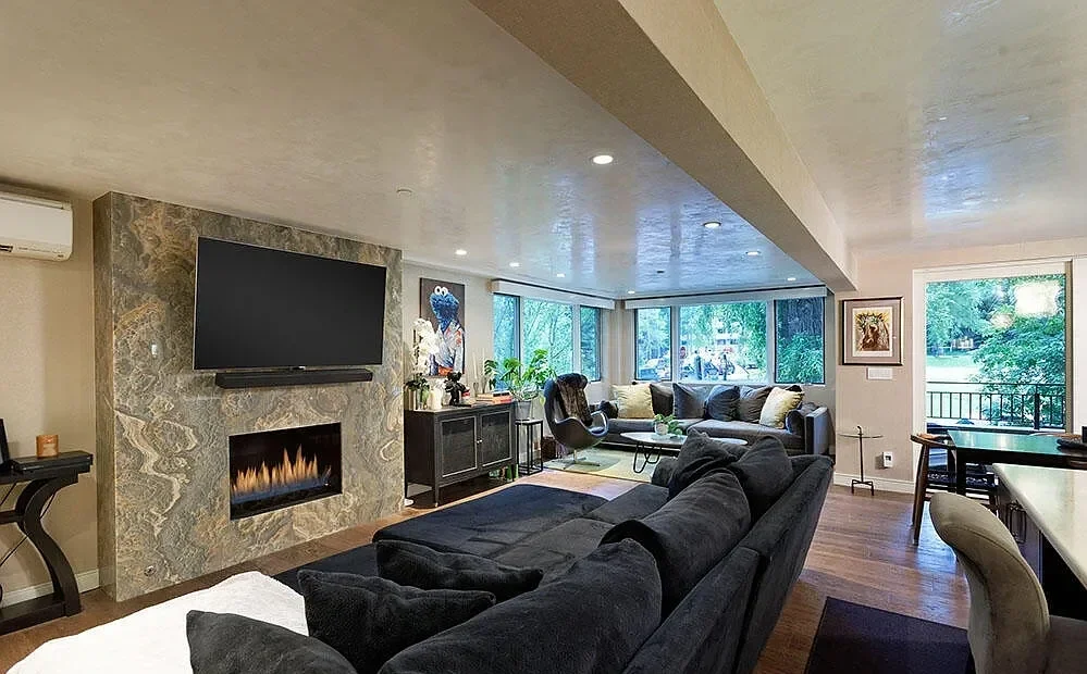 Modern luxury living room featuring a marble-clad linear fireplace and floor-to-ceiling windows in Aspen, Colorado.