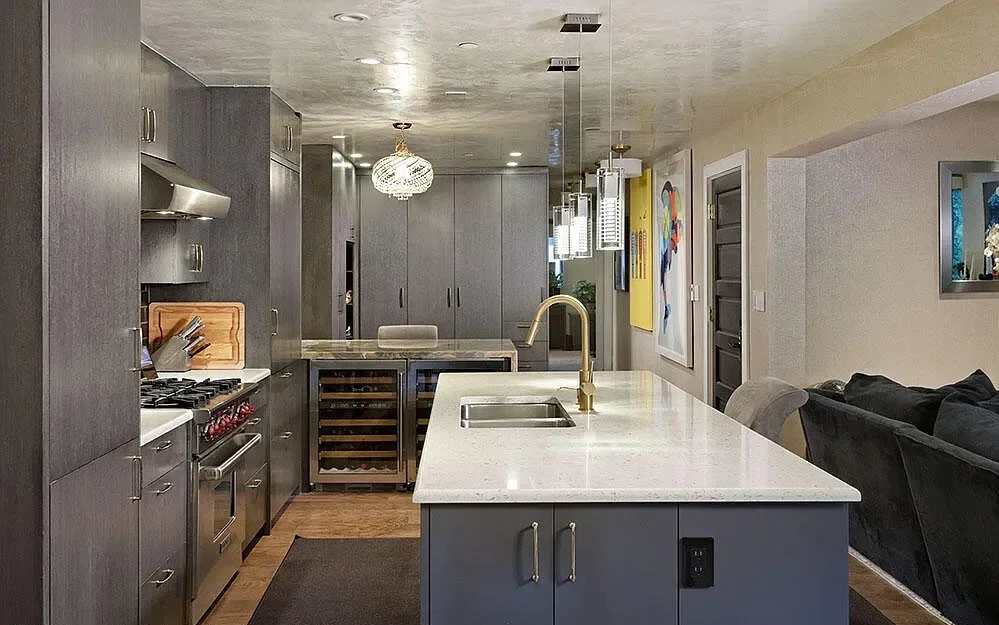 Sleek contemporary kitchen with charcoal gray cabinetry, white quartz countertops and center island, brass gold faucet, and built-in wine coolers in Aspen, Colorado.