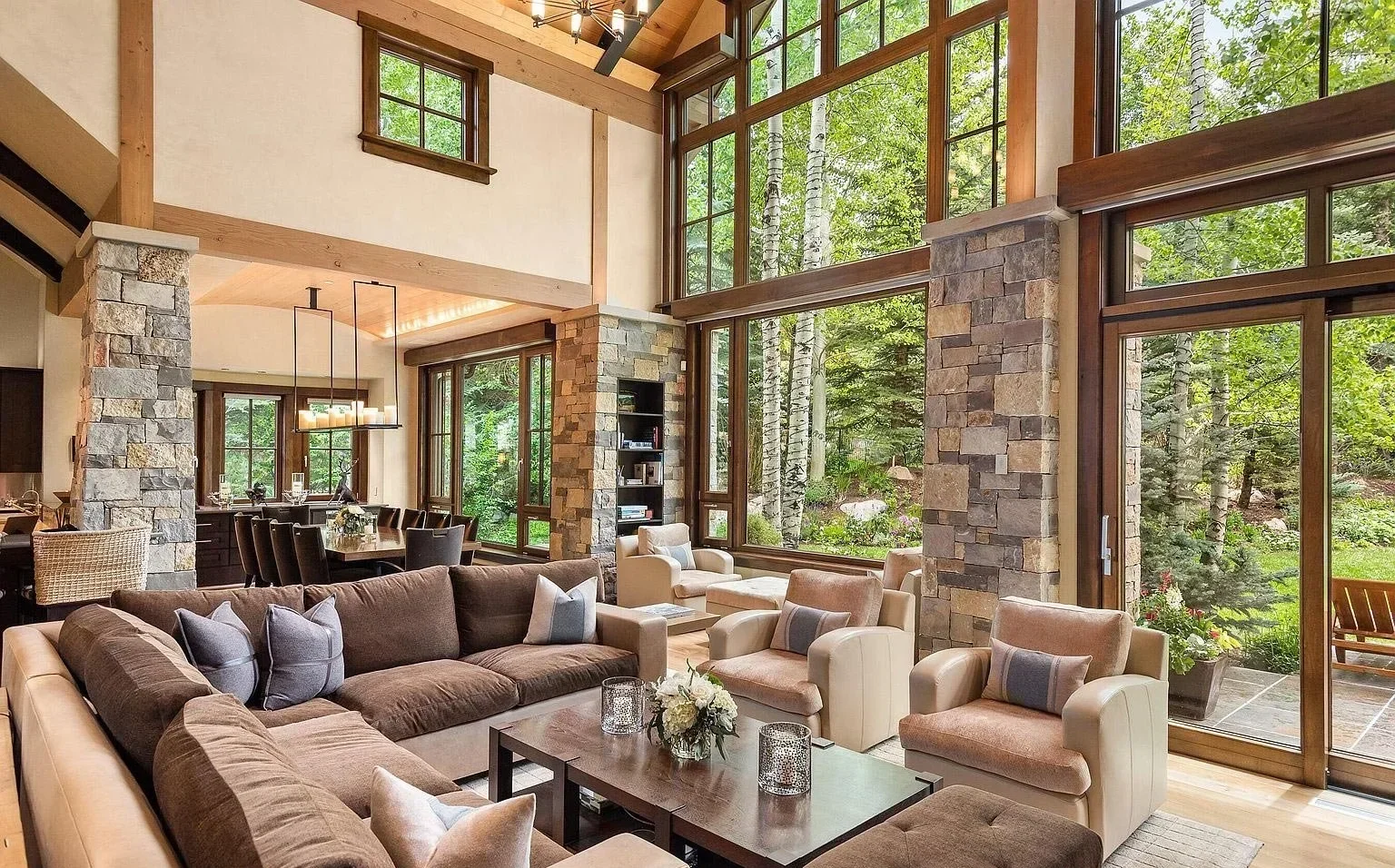A luxurious living and dining room with stone walls, vaulted ceilings, and floor-to-ceiling windows built by John Olson, owner of Form 44 Construction, on Crystal Lake Road in Aspen, Colorado.