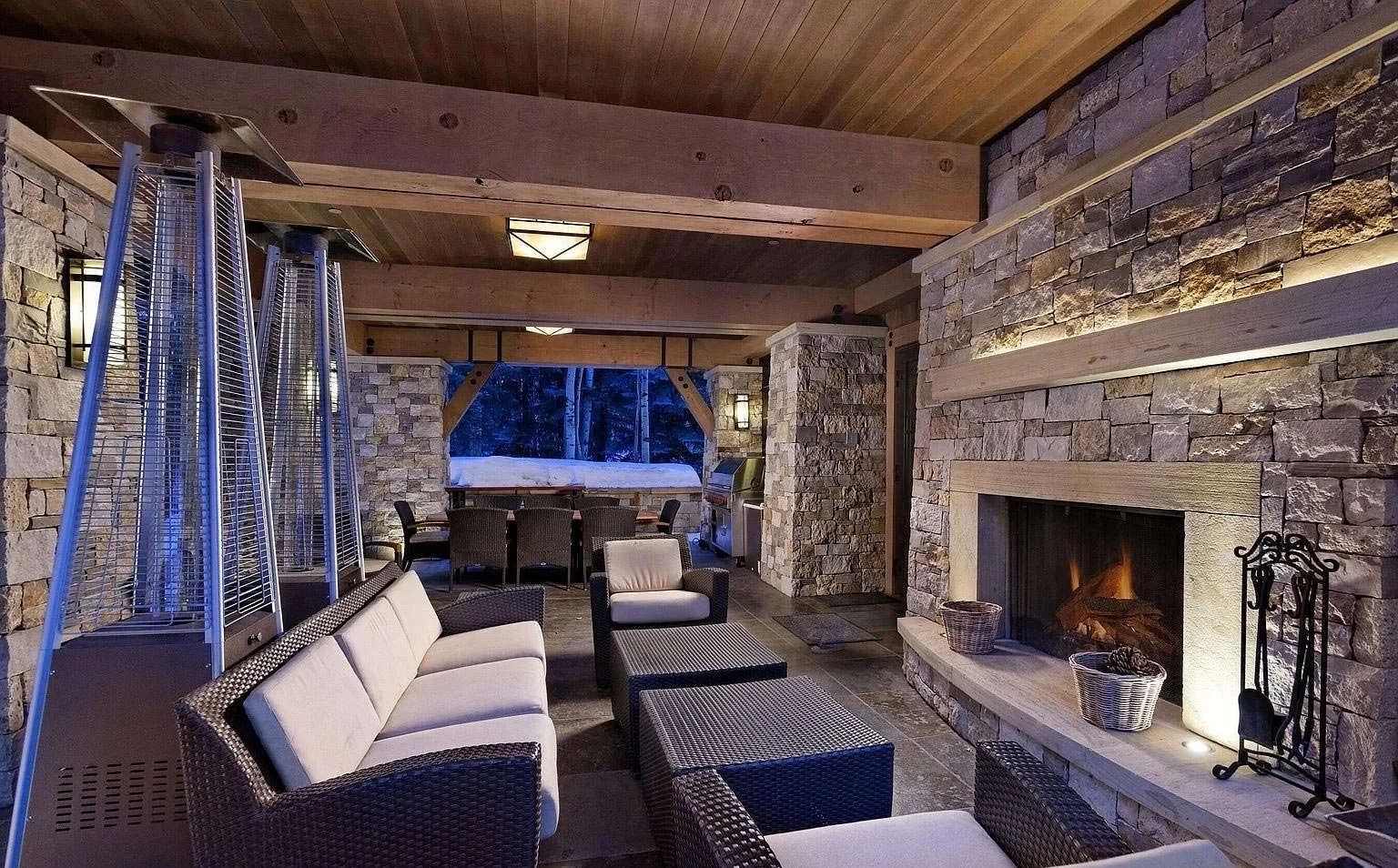 Luxurious covered outdoor patio with stacked stone fireplace, exposed wood ceiling beams, and built-in lighting, built by John Olson, owner of Form 44 Construction, on Crystal Lake Road in Aspen, Colorado.