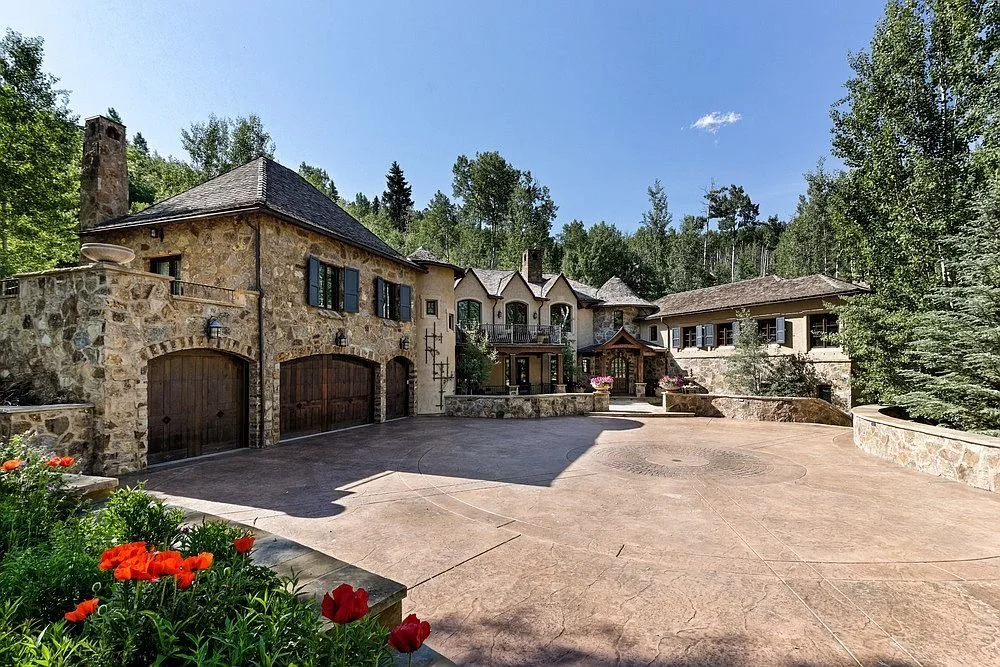 A spacious stone home with a driveway and beautiful flower beds in front surrounded by tall pines and aspen trees built by John Olson, owner of Form 44 Construction, on Spruce Ridge Lane in Snowmass Village, Colorado.