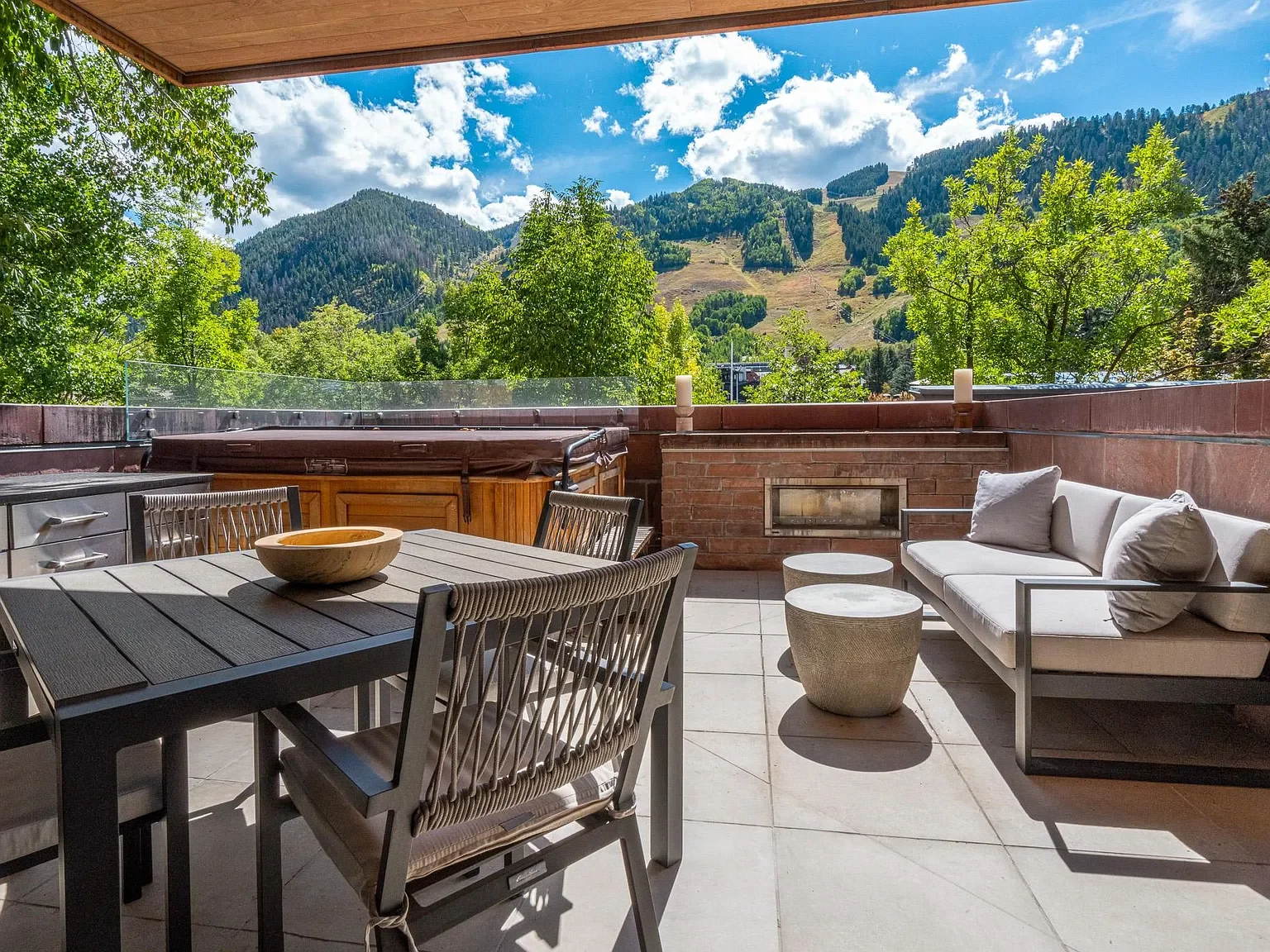 Private outdoor terrace featuring a hot tub, outdoor fireplace, and ski mountain views at The Mother Lode in Aspen, Colorado.