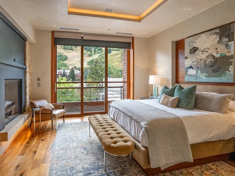 Modern luxury bedroom with custom fireplace, cove ceiling lighting, and direct ski mountain views at The Mother Lode in Aspen, Colorado.