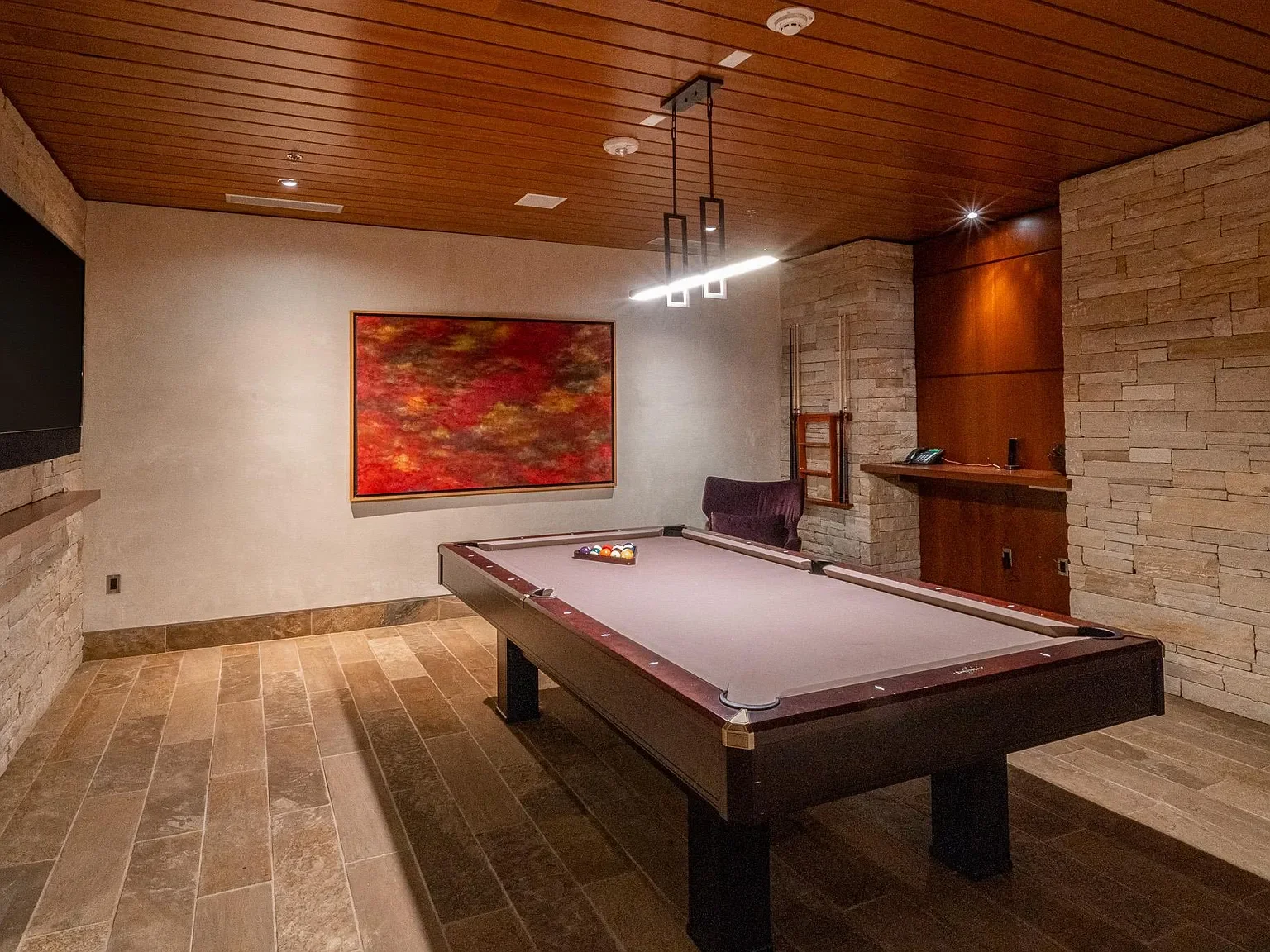 Luxury billiards lounge and entertainment room featuring stacked stone walls and custom slatted ceilings at The Mother Lode in Aspen, Colorado.