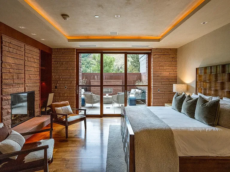 Luxury bedroom suite with custom stone fireplace, tray ceiling lighting, and patio views at The Mother Lode in Aspe, Colorado.
