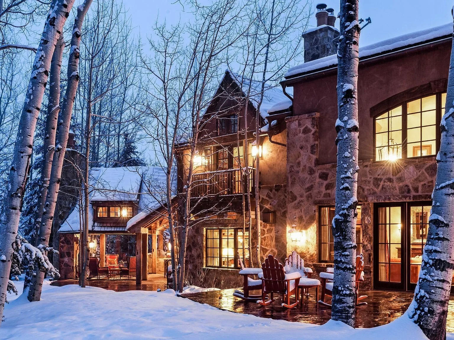 A spacious, brightly lit stone house nestled amidst snow covered aspen trees, creating a serene and picturesque setting built by John Olson, owner of Form 44 Construction, on Spruce Ridge Lane in Snowmass Village, Colorado.