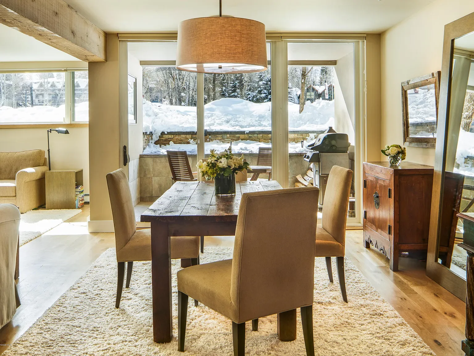 Modern rustic dining room with a wooden dining table, drum pendant light, and sliding glass doors with snow-covered patio views in Aspen, Colorado.