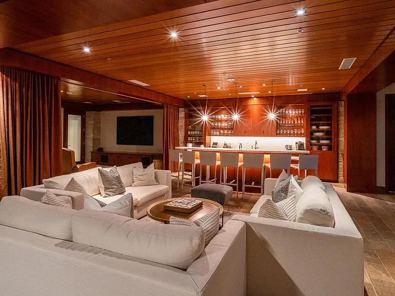 Custom wood-paneled entertainment lounge featuring a full bar, illuminated glassware displays, and rich wood slat ceilings at The Mother Lode in Aspen, Colorado.