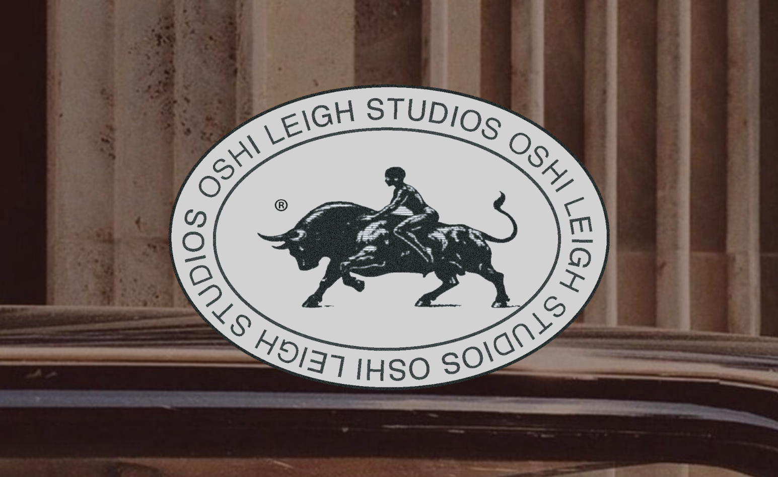 A logo for Oshii Leigh Studios featuring a woman riding a charging bull inside an oval with the studio's name repeated around it, set against a background of wooden wall paneling.