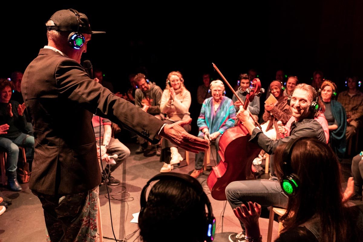 Muziekoptreden met artiest die gitaar speelt en publiek dat geniet, allemaal met koptelefoons op