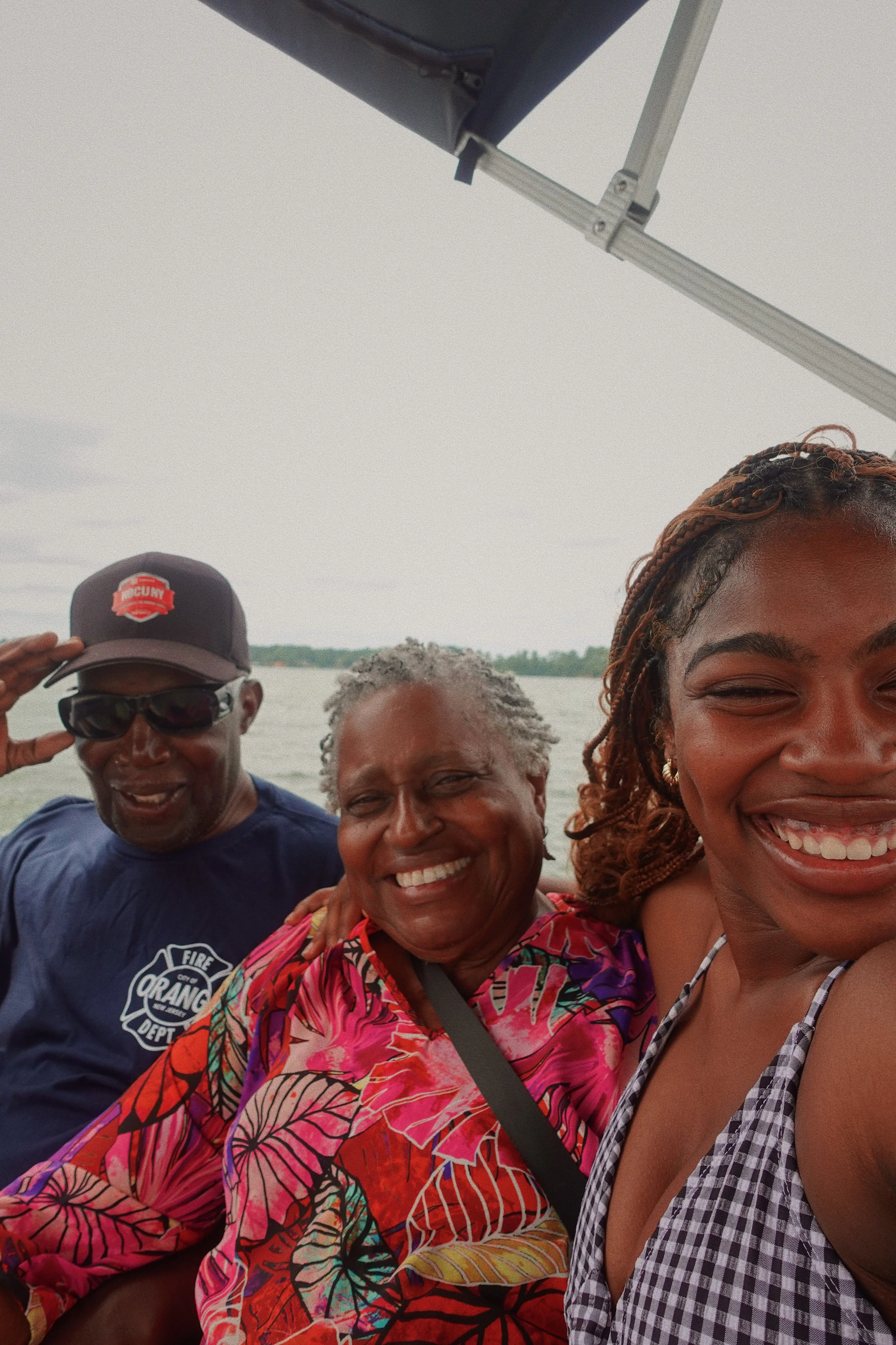 Morgan J. Hackett and grandparents on a boat near the water with a cloudy sky in the background, wearing casual summer clothes and hats.