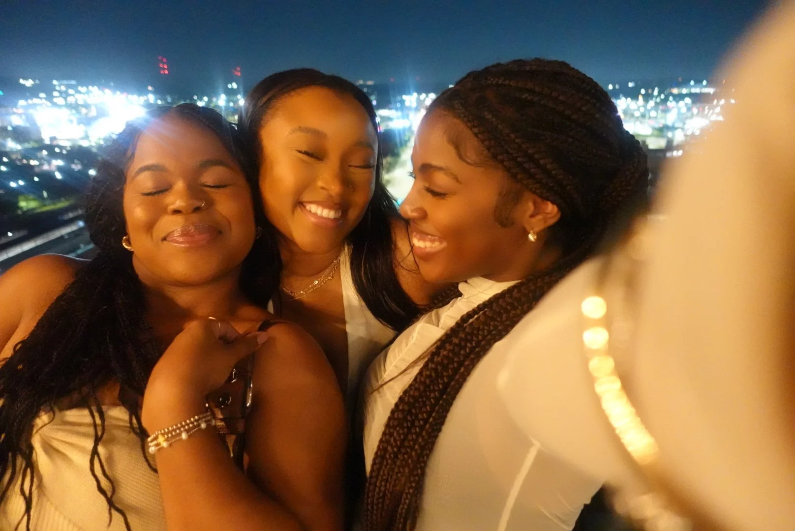 Morgan J. Hackett and friends are smiling and embracing Birmingham at night with city lights in the background.