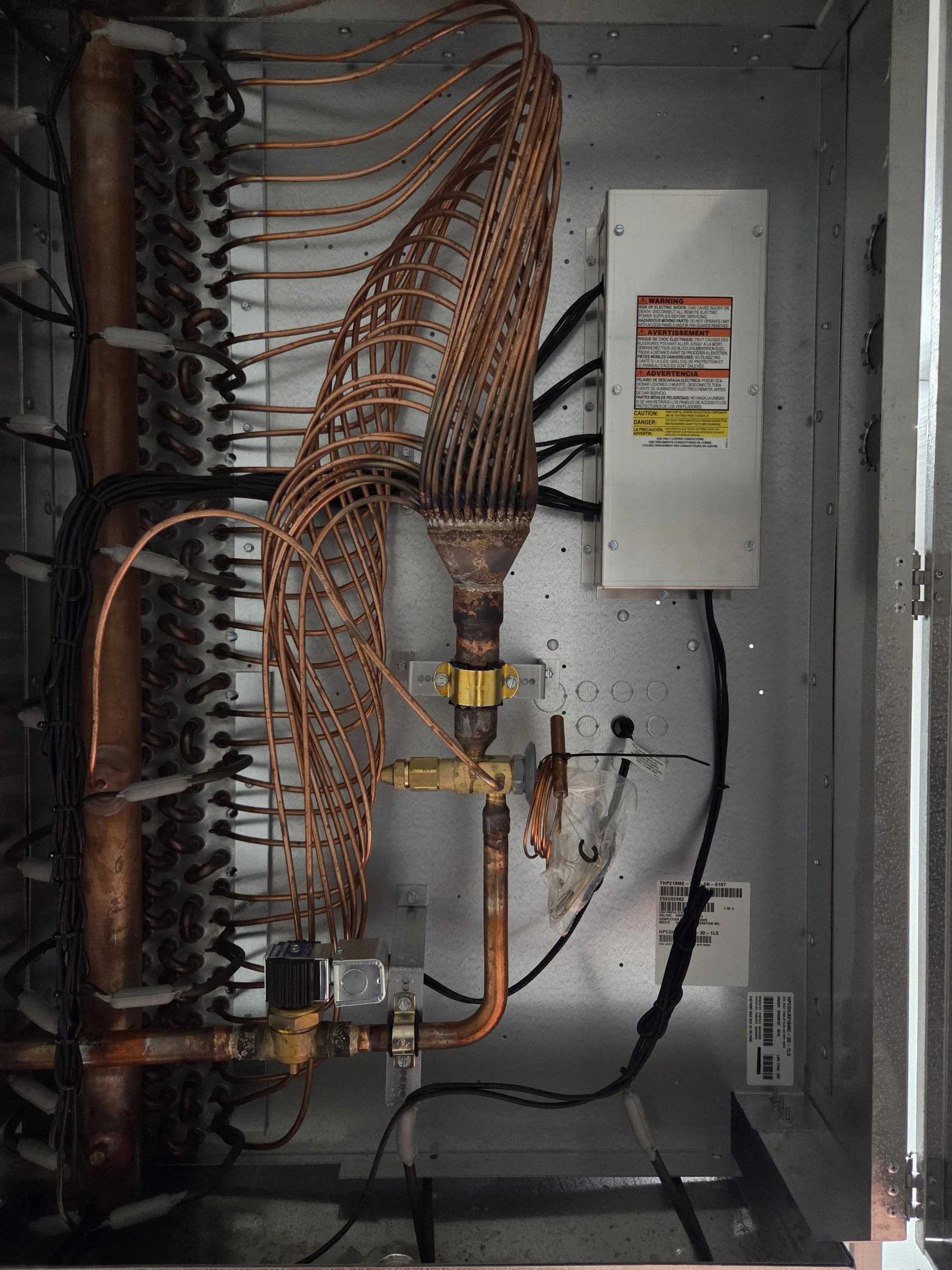 Interior of an electrical or HVAC control panel with copper wiring, metal components, and warning labels.