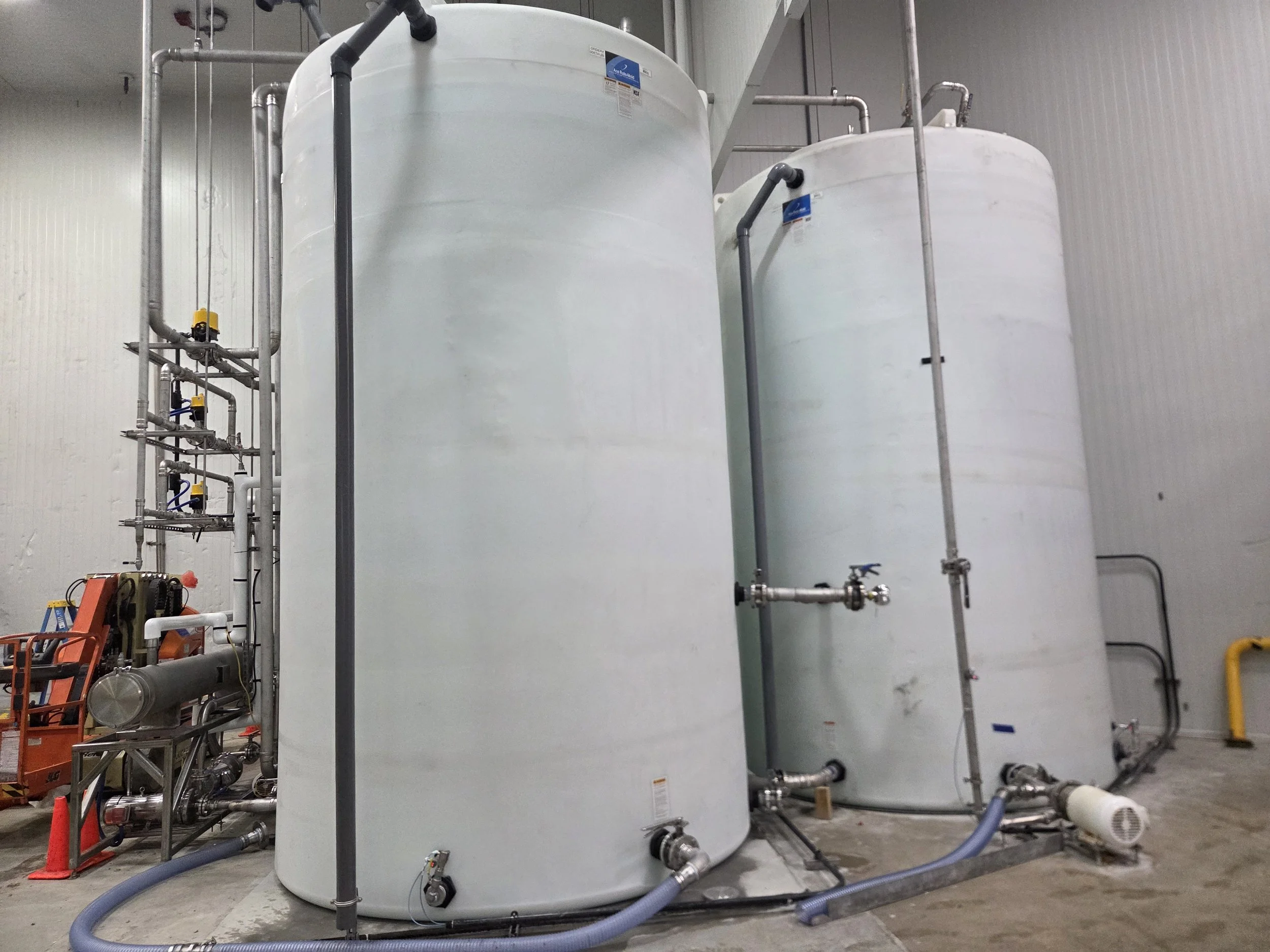 Two large white tanks with piping and valves in an industrial setting.