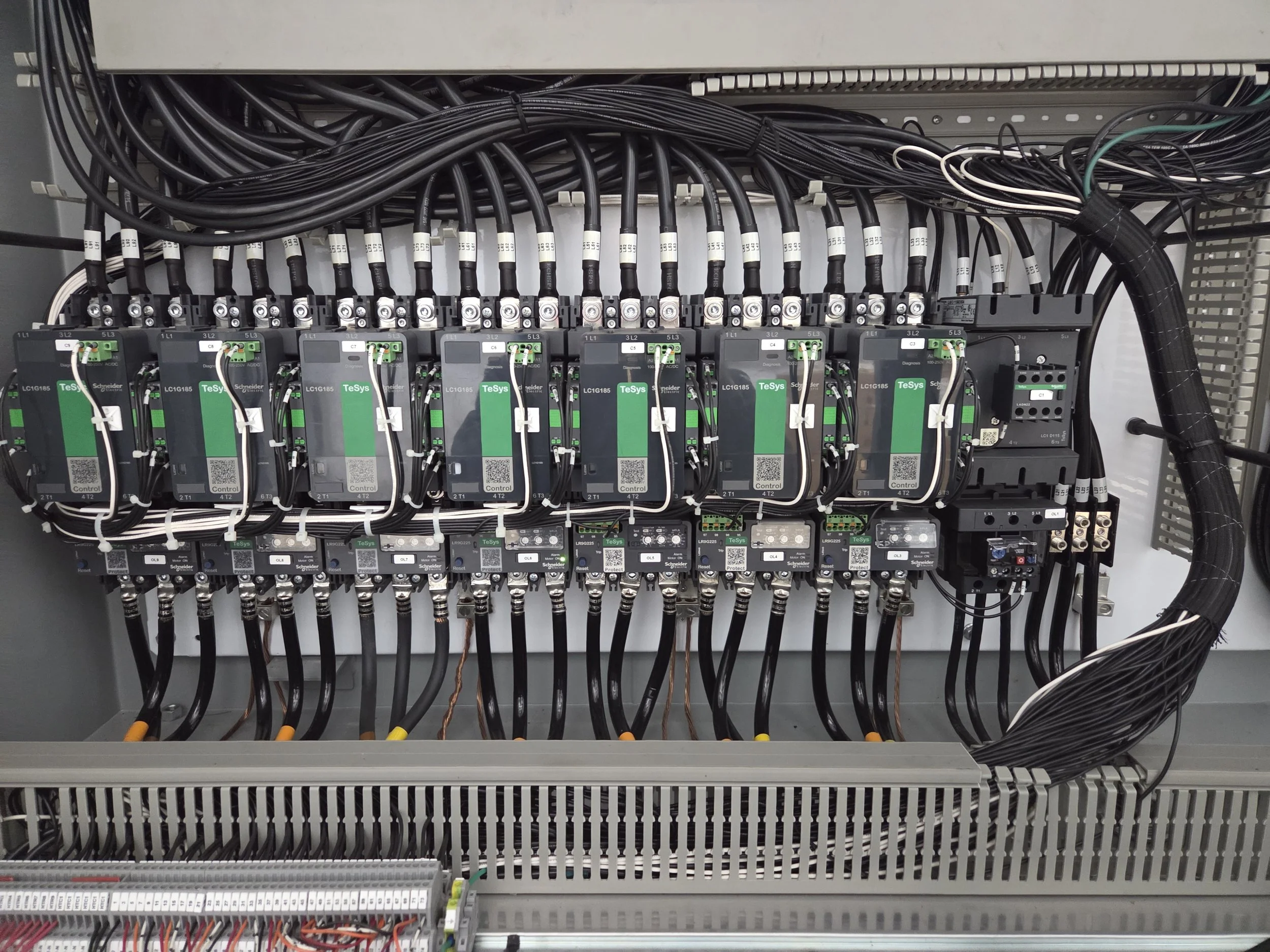 An electrical control panel with numerous black cables connected to various circuit breakers and components.