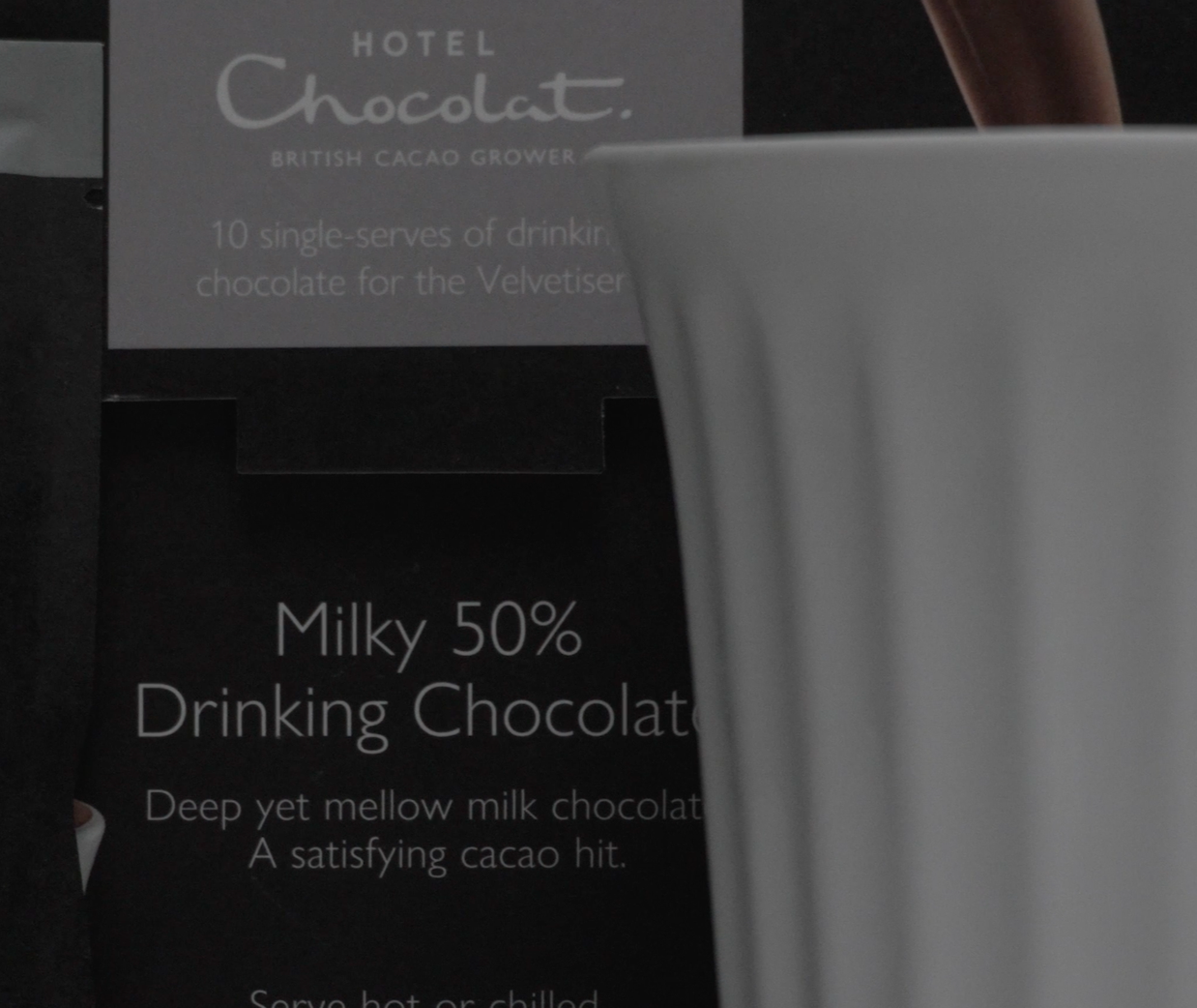 Close-up of a sign with text about a Milky 50% drinking chocolate product, partially obscured by a white cup in the foreground.
