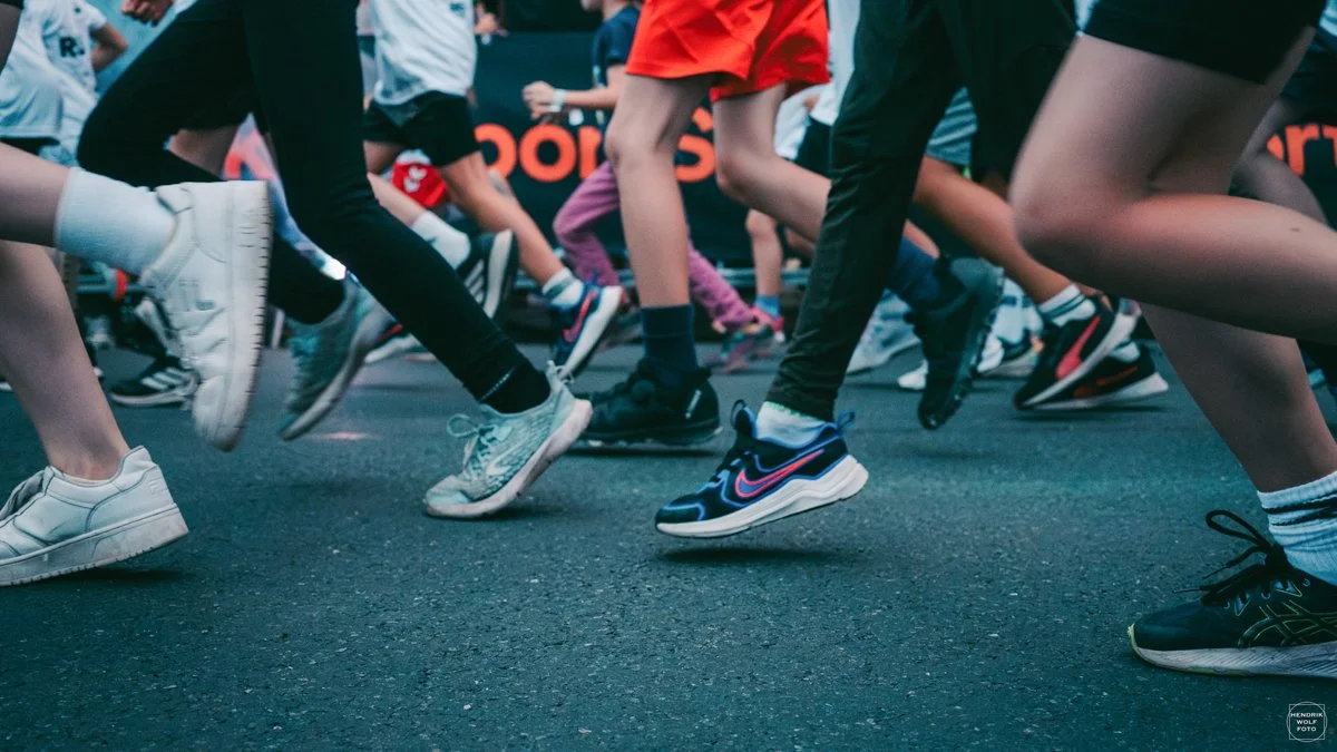 Close-up of multiple people running, focusing on their legs and shoes, during a race or marathon.