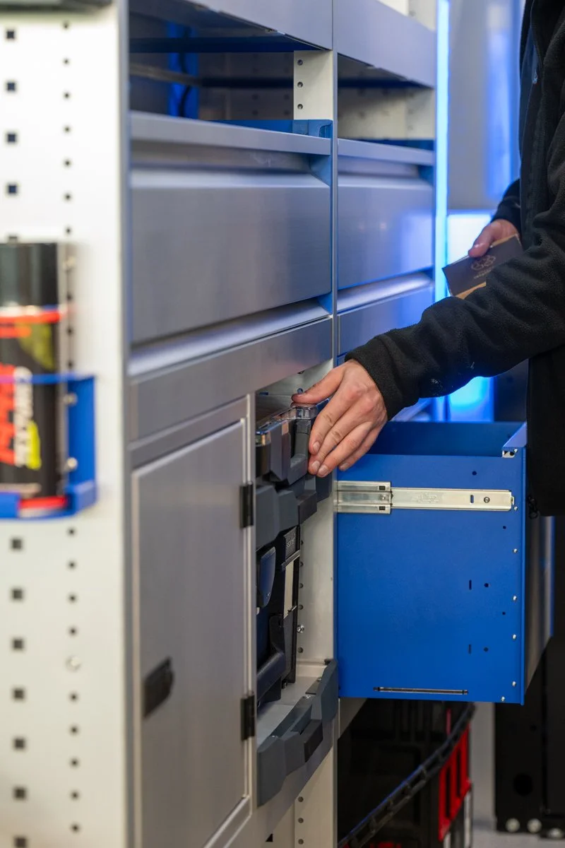 Person opening a blue and gray storage cabinet in a workshop or industrial setting.