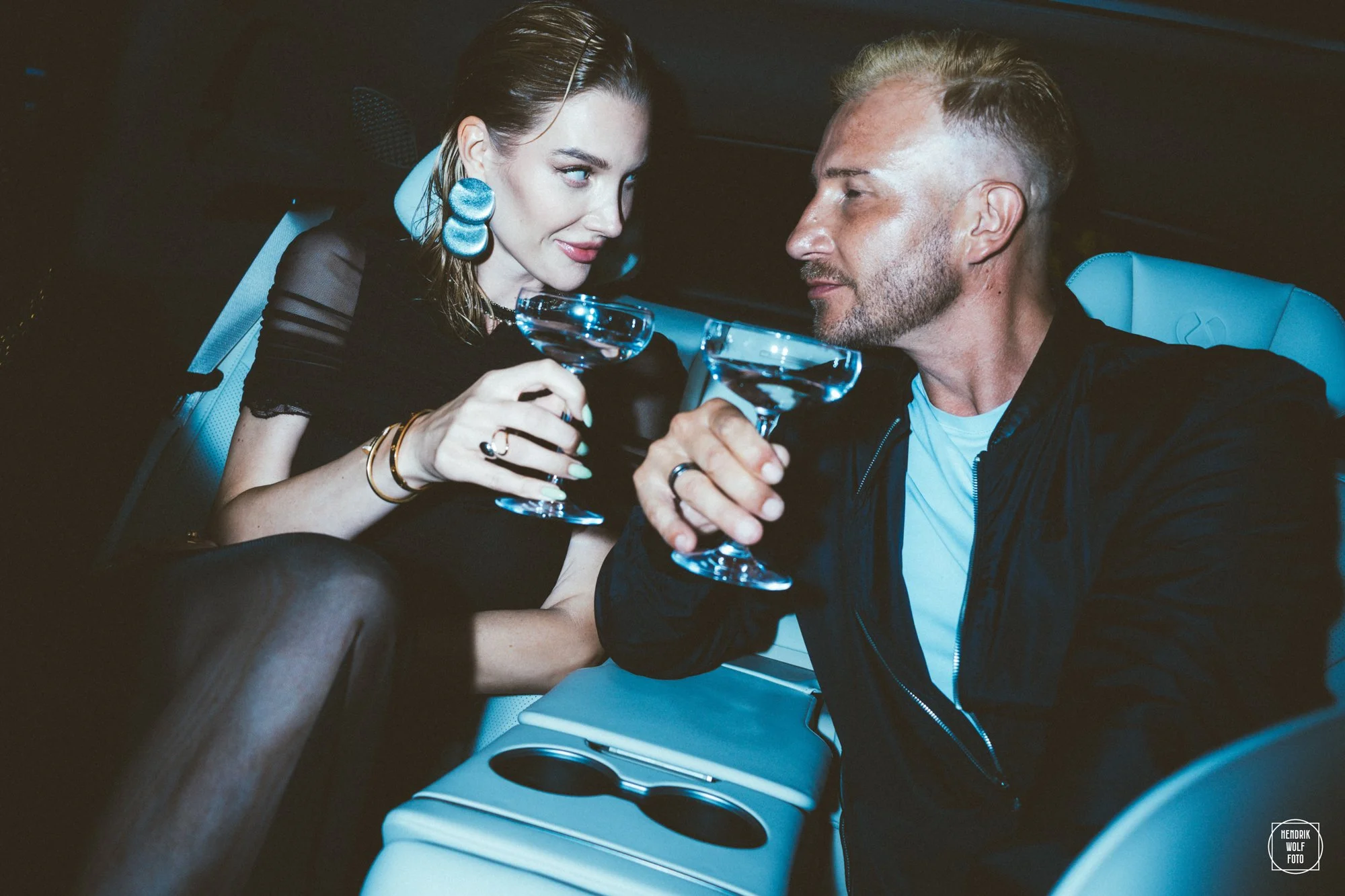 A woman and a man sitting in a car at night, clinking champagne glasses together, close-up shot.