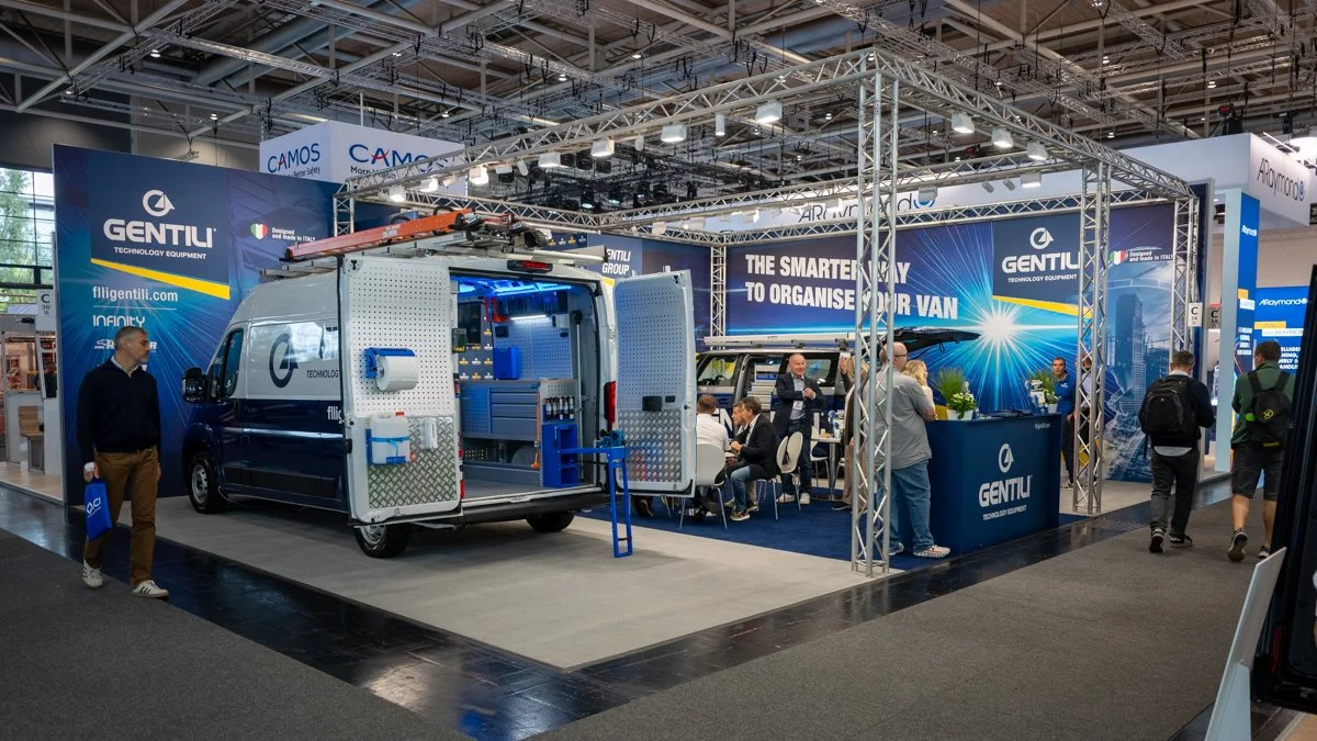 Exhibition booth at a trade show featuring a converted van with storage and equipment, branded with Gentili, displaying tools and organization solutions with several people engaging and walking around.