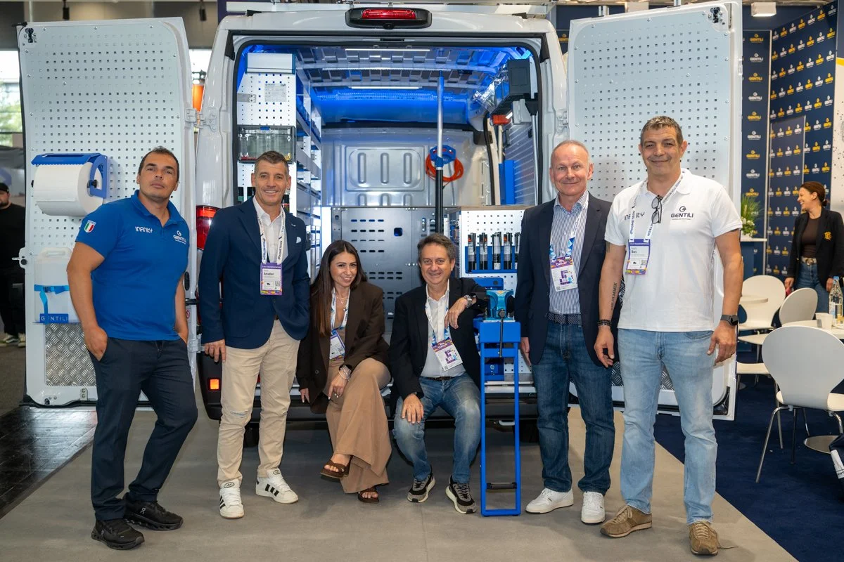 Group of six people standing in front of an open vehicle or mobile lab at an exhibition or conference.