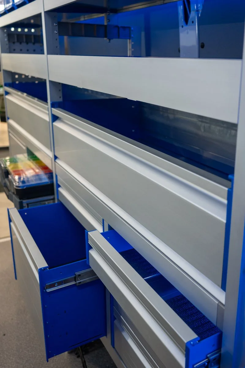Blue and white industrial shelving unit with multiple empty storage compartments, some drawers partially open, in a retail or warehouse setting.