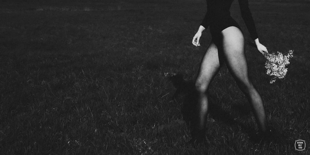 Black and white photo of a woman holding a bouquet of flowers, walking on grass at night.