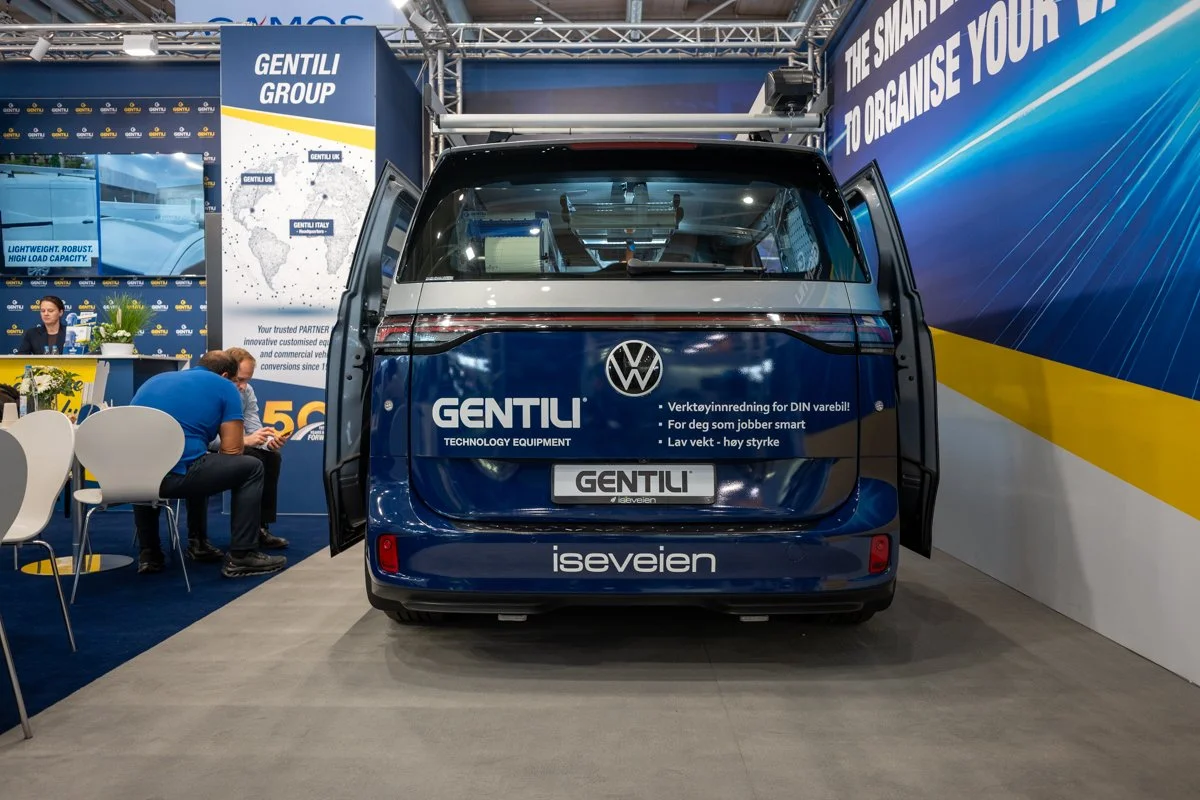 Back view of a Volkswagen electric van at an exhibition, displaying branding for Gentili Technology Equipment and Isevein, with open rear doors and signage about vehicle customization and working smart.