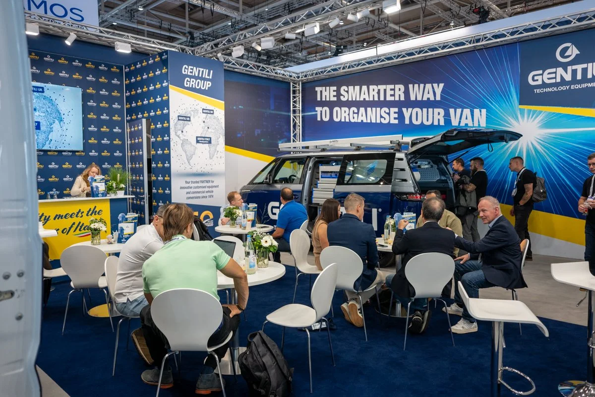 Trade show booth for Gentili Group showcasing vehicle organization solutions, featuring a van with equipment, a large backdrop with the text 'The smarter way to organise your van', and attendees engaging in discussions.