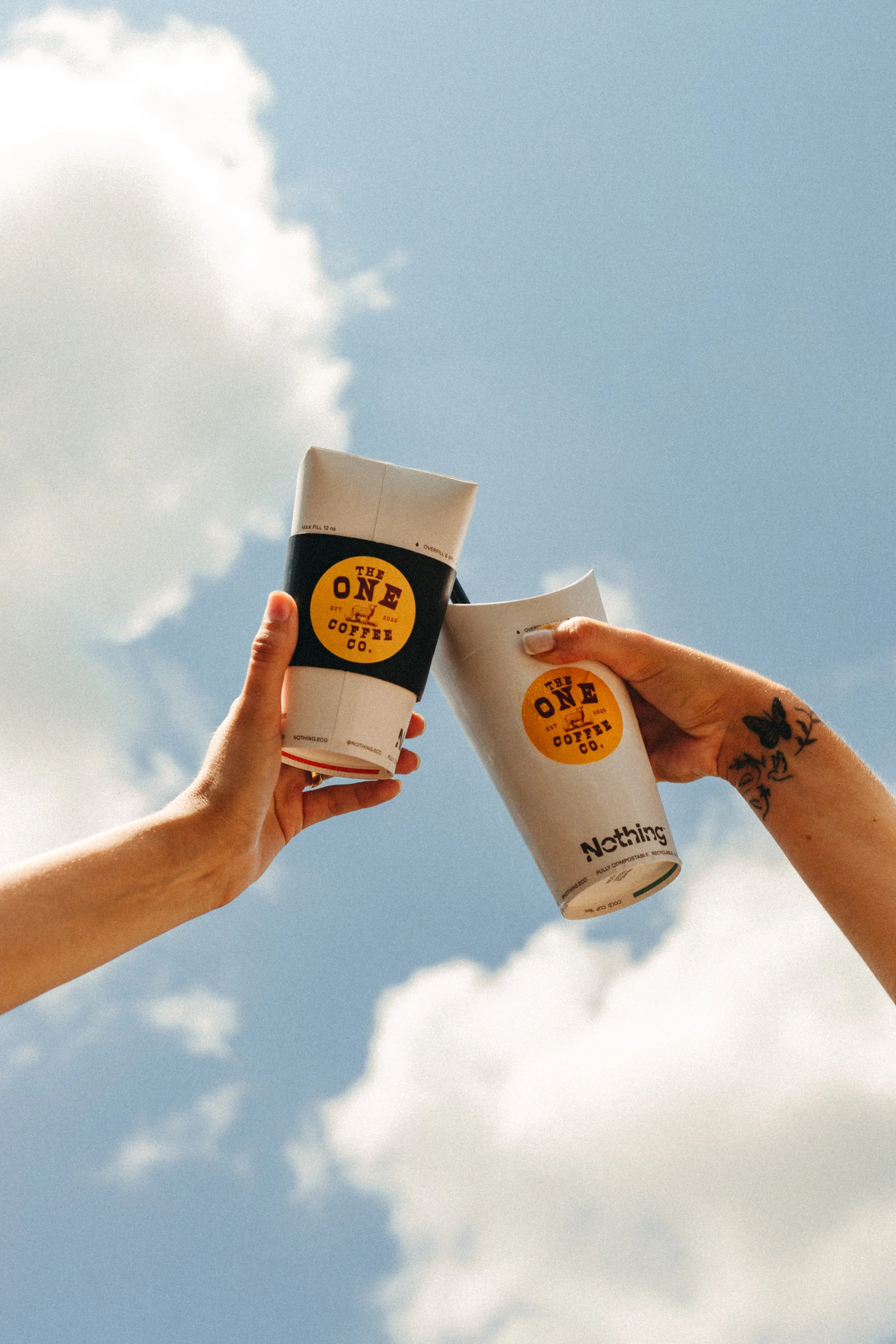 Three people holding cups of coffee against a blue sky with clouds.
