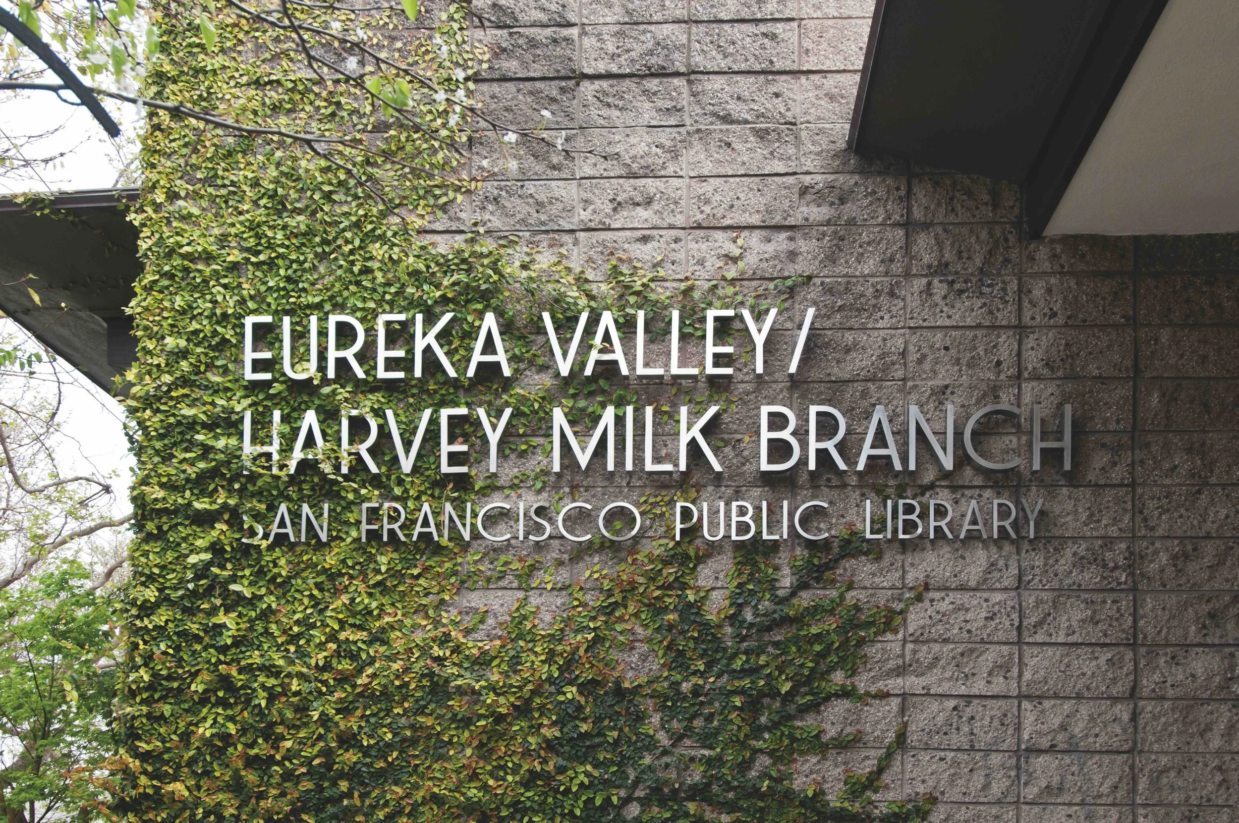 Sign for Eureka Valley Harvey Milk Branch at San Francisco Public Library with green foliage covering part of the brick wall.
