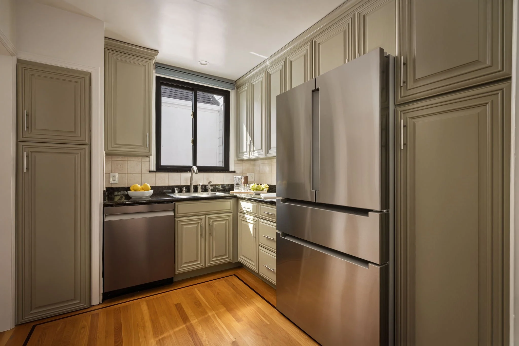 Kitchen with beige cabinets, stainless steel refrigerator, and black granite countertops. There is a window above the sink.