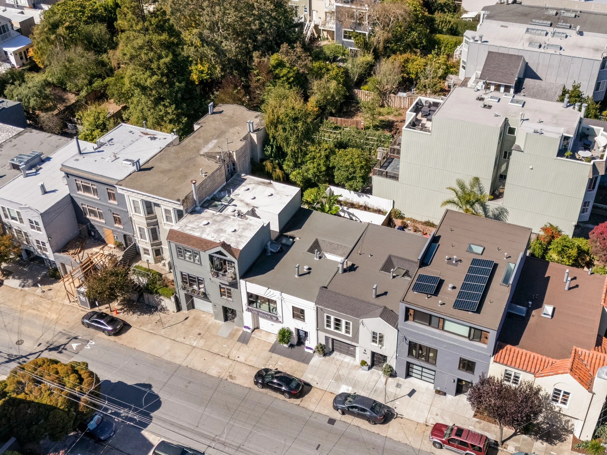 Bird's-eye view of a city neighborhood with multi-story residential buildings, trees, sidewalks, parked cars, and a street with electrical lines.