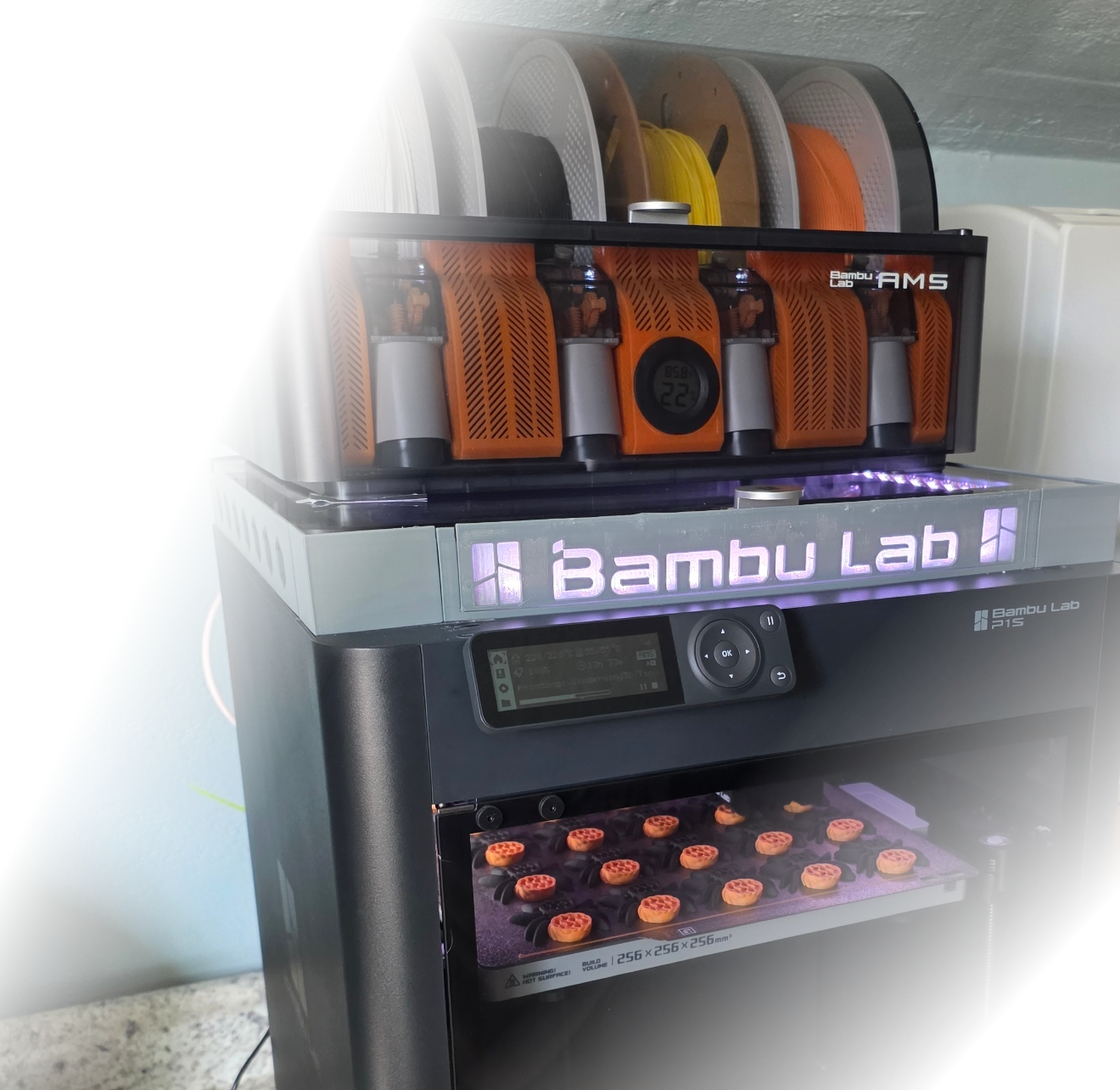 A 3D printer with a display screen prints small orange and black Halloween-themed prints.