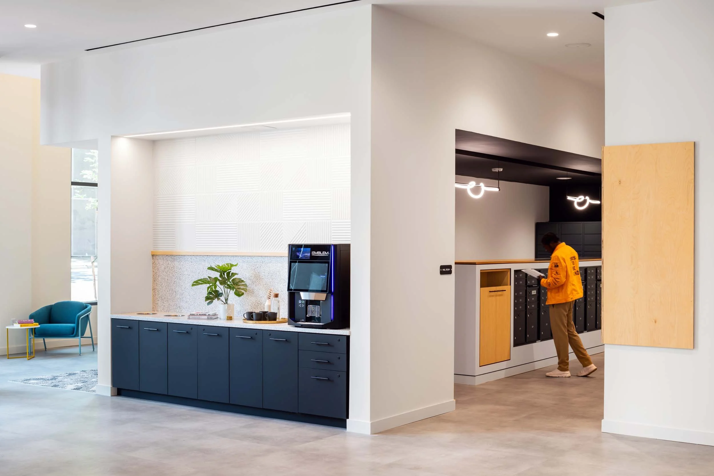 Modern lobby area with a seating arrangement, coffee station, and a person at mail lockers.