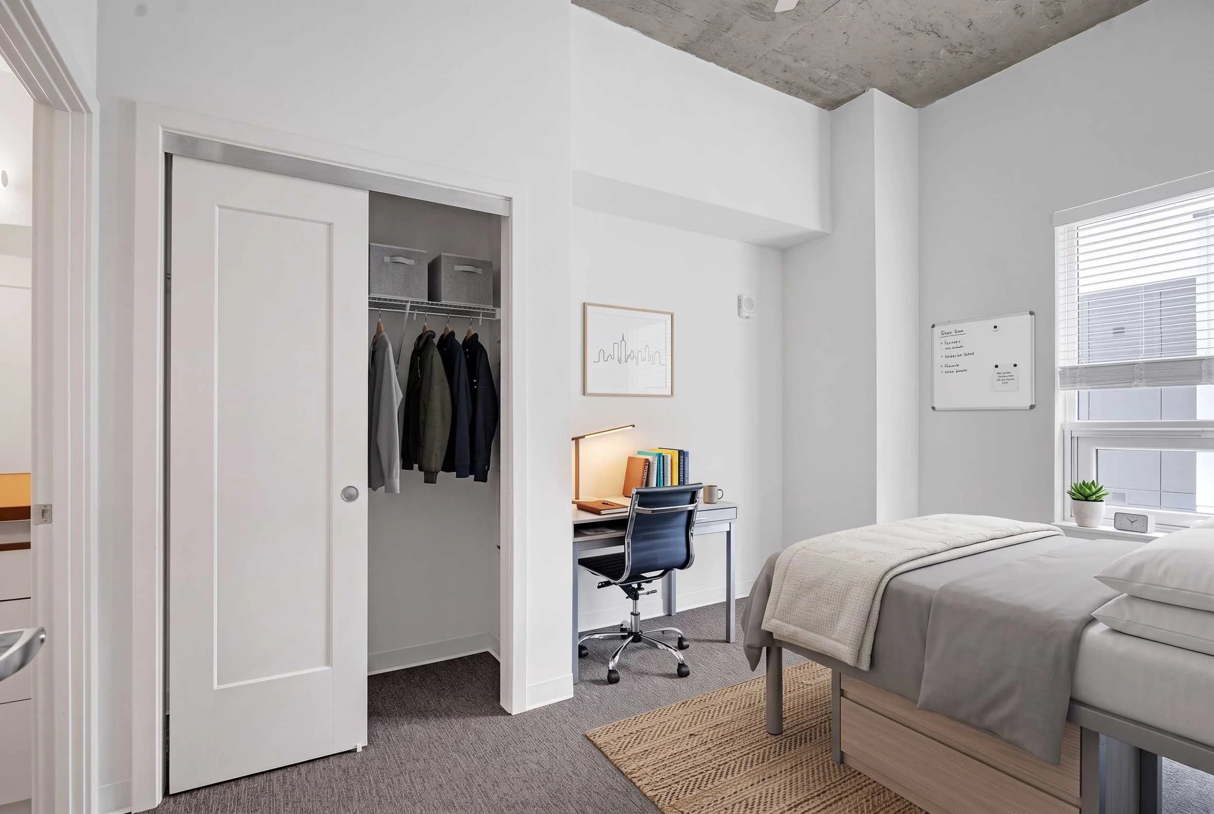 A modern bedroom with white walls, a bed with white bedding, a small desk with a chair, a window with blinds, a potted plant, and a whiteboard on the wall.