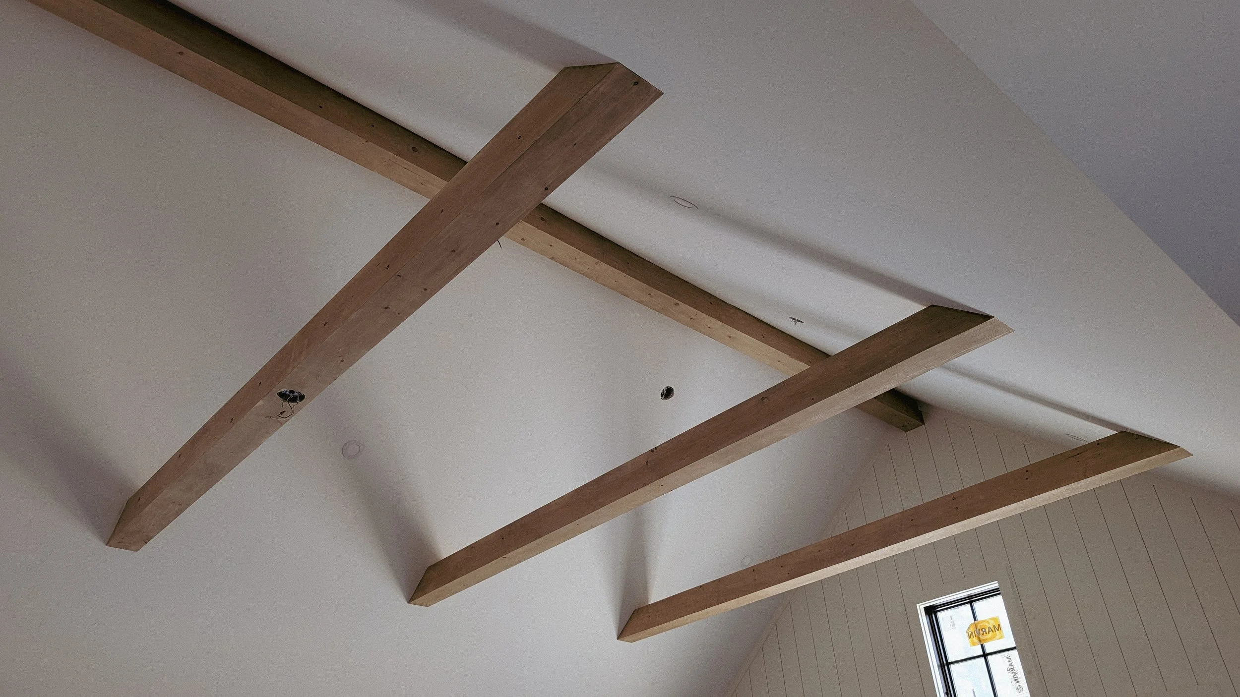 Wooden beams installed on a ceiling with a window visible below.