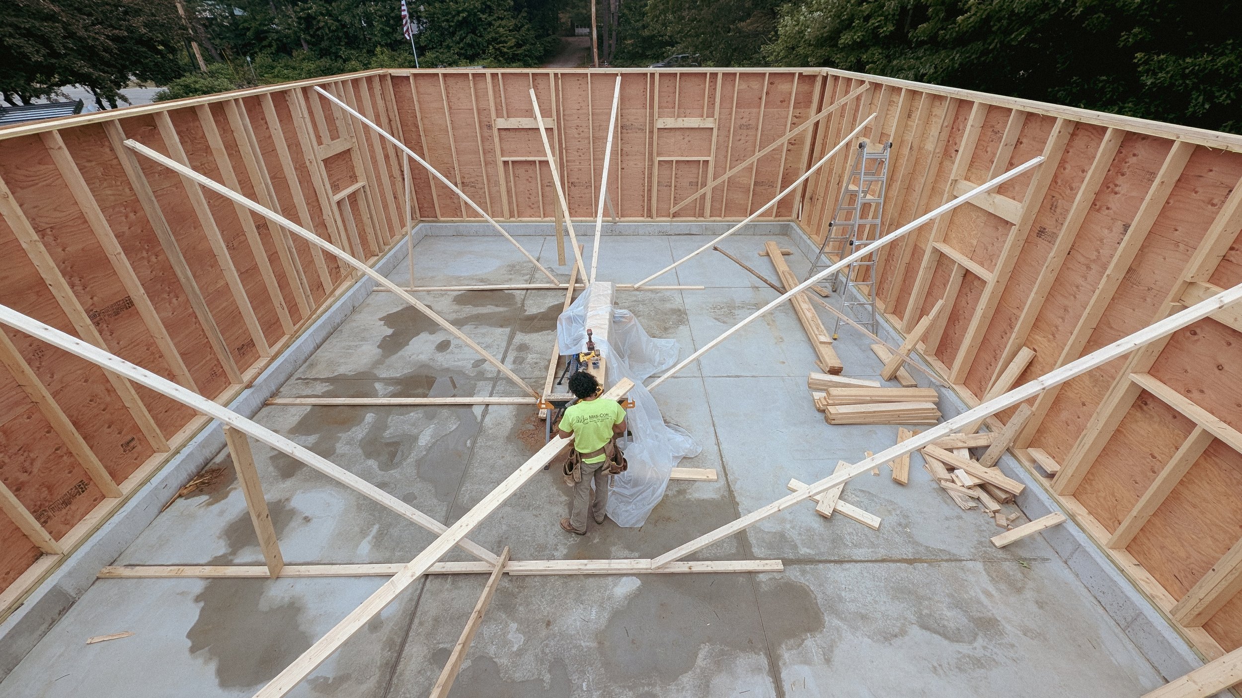 Construction site with wooden framing and two workers working on a concrete floor.