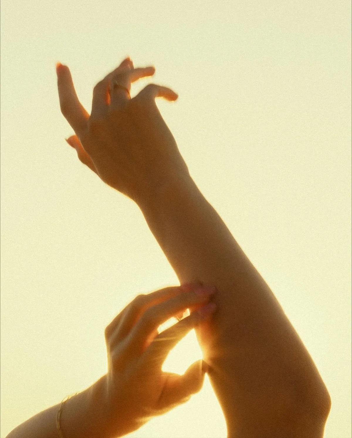 Multiple hands reaching upward against a bright, soft yellow background, illuminated by sunlight.