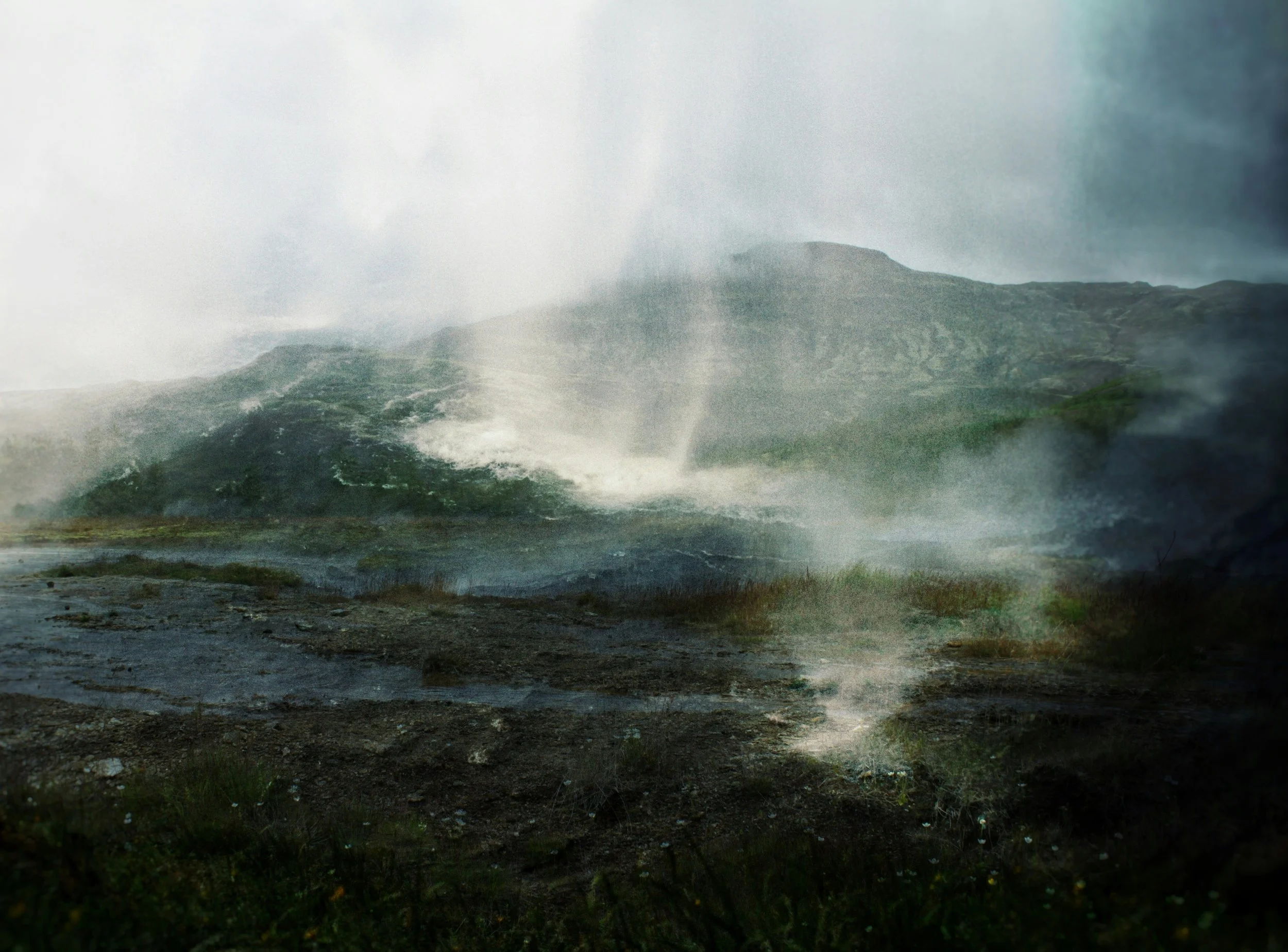 A landscape scene with mountains in the background, fog, a body of water, and greenery in the foreground.