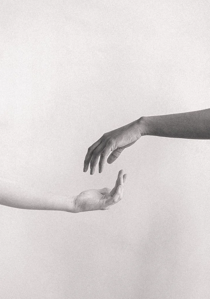 Two hands reaching towards each other, one slightly above the other, in a minimalist black-and-white photo.