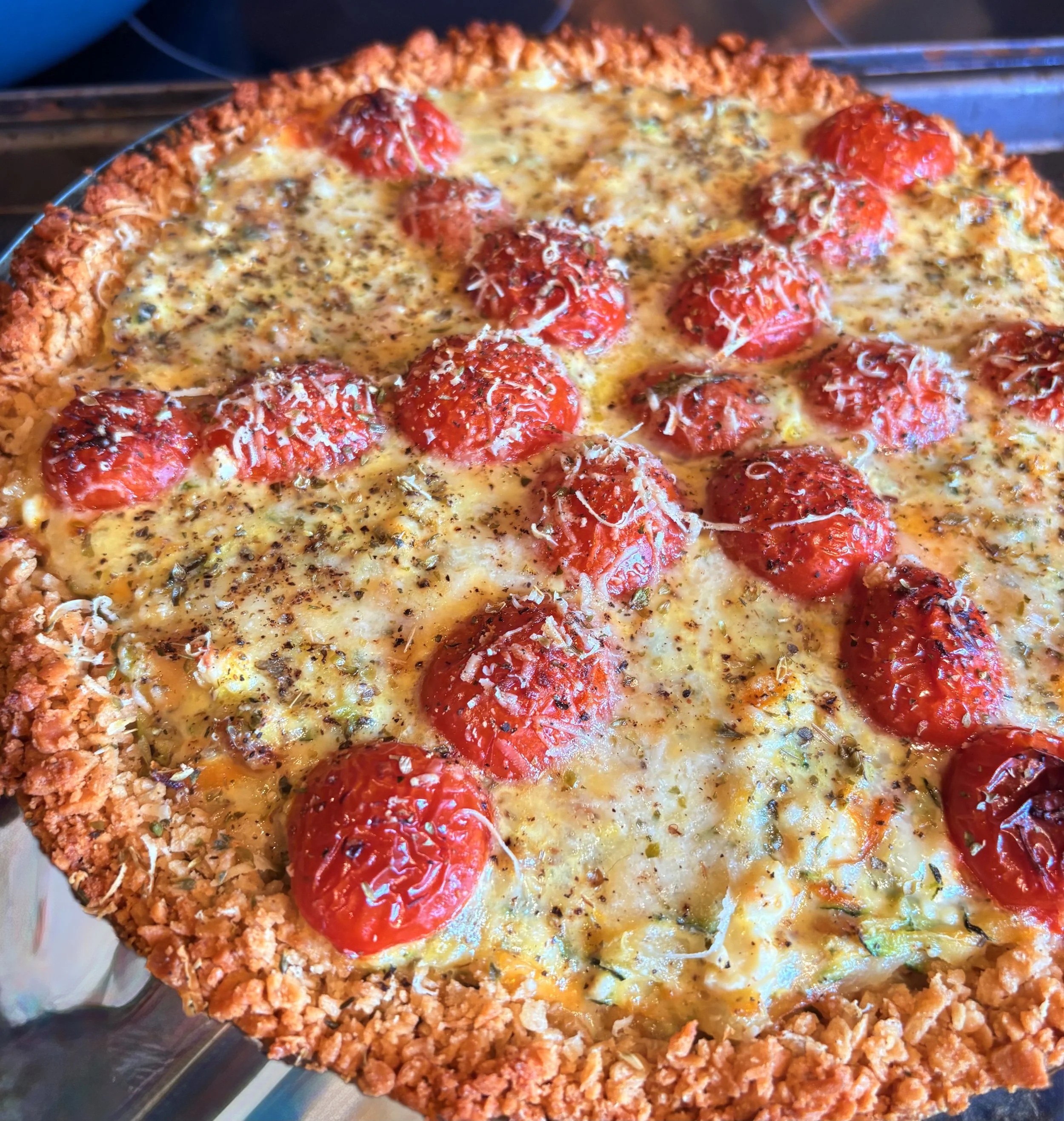 Close-up of a freshly baked pizza with a crust coated in crushed crackers, topped with melted cheese, toy-like meatballs, and herbs.